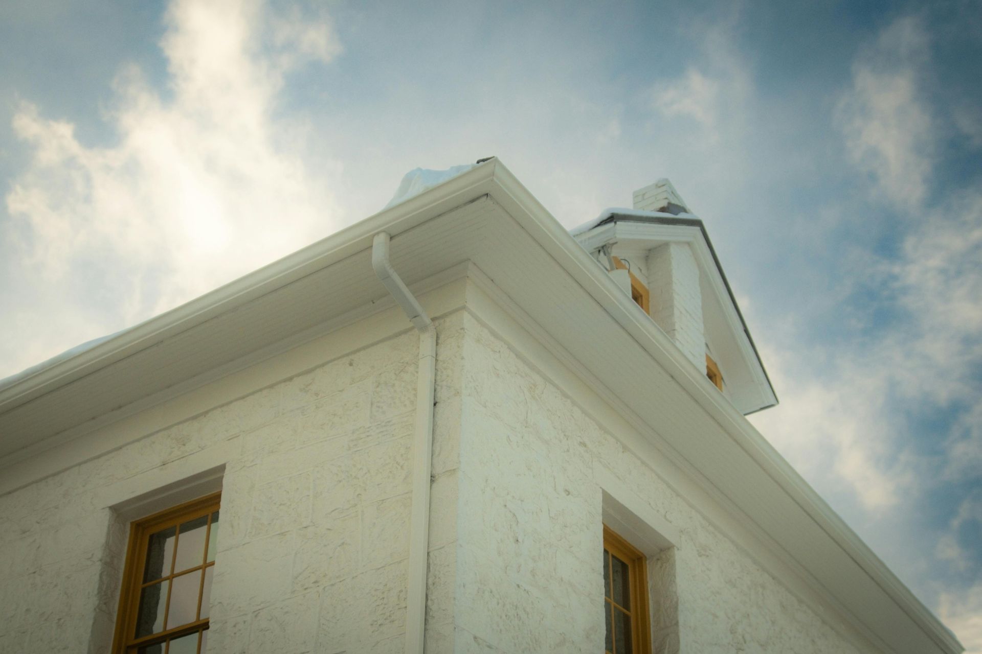 White stucco building corner with wooden windows and a cloudy sky above