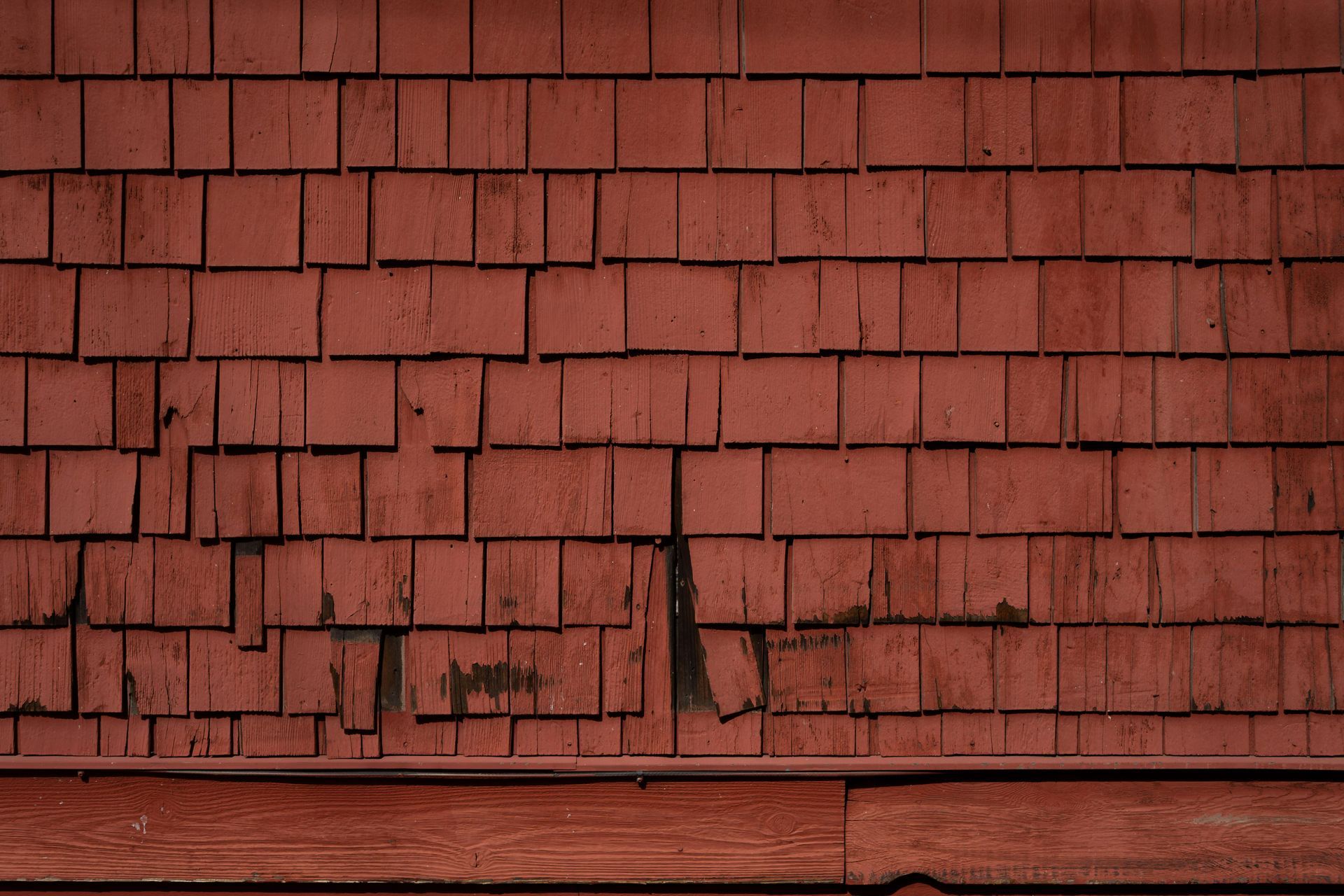 Red wooden shingle wall with a narrow horizontal trim at the bottom