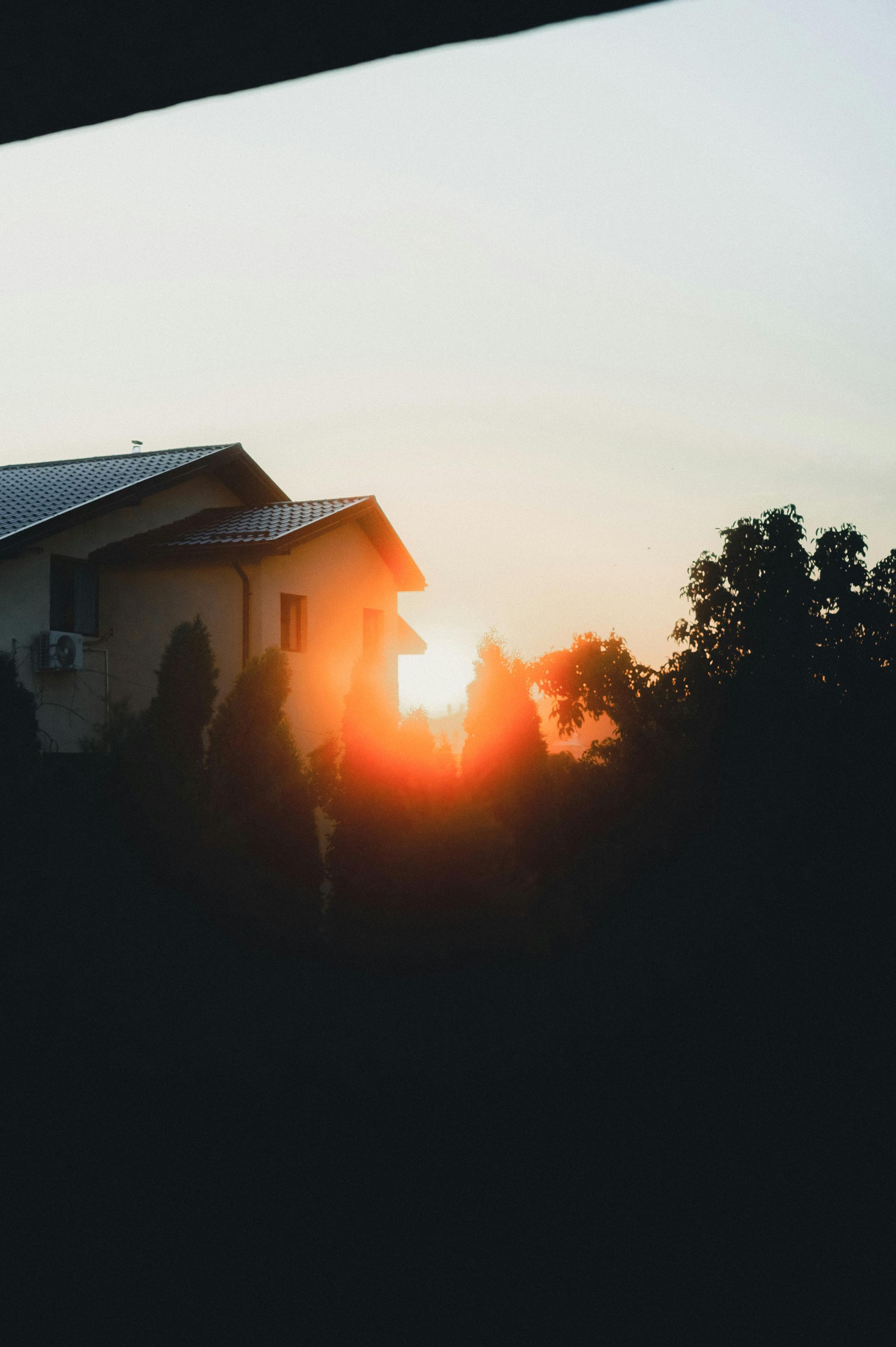 Sunset behind a house silhouette, with dark trees and a bright orange glow in the sky.