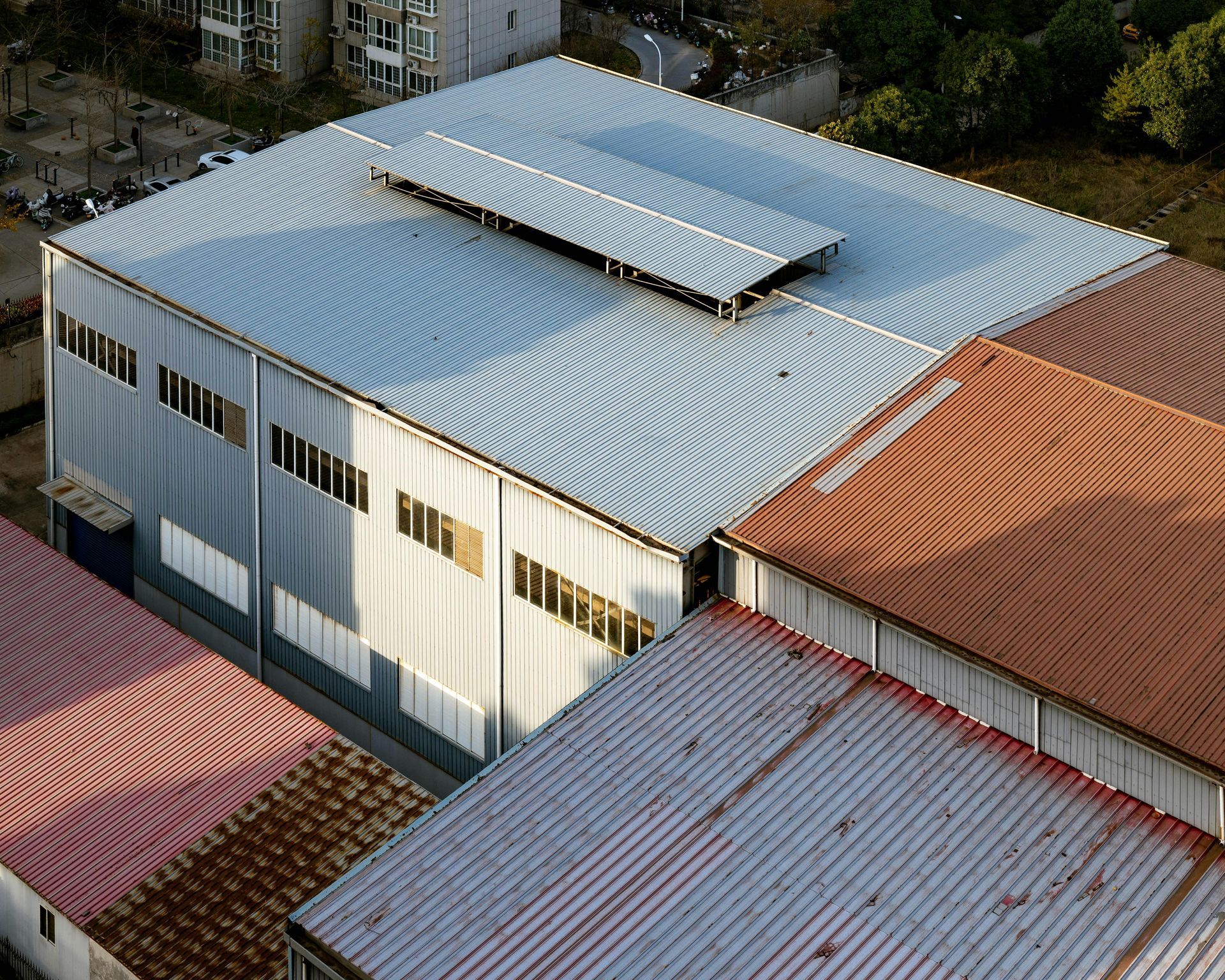 Aerial view of a white industrial building with a curved metal roof among red-roofed buildings