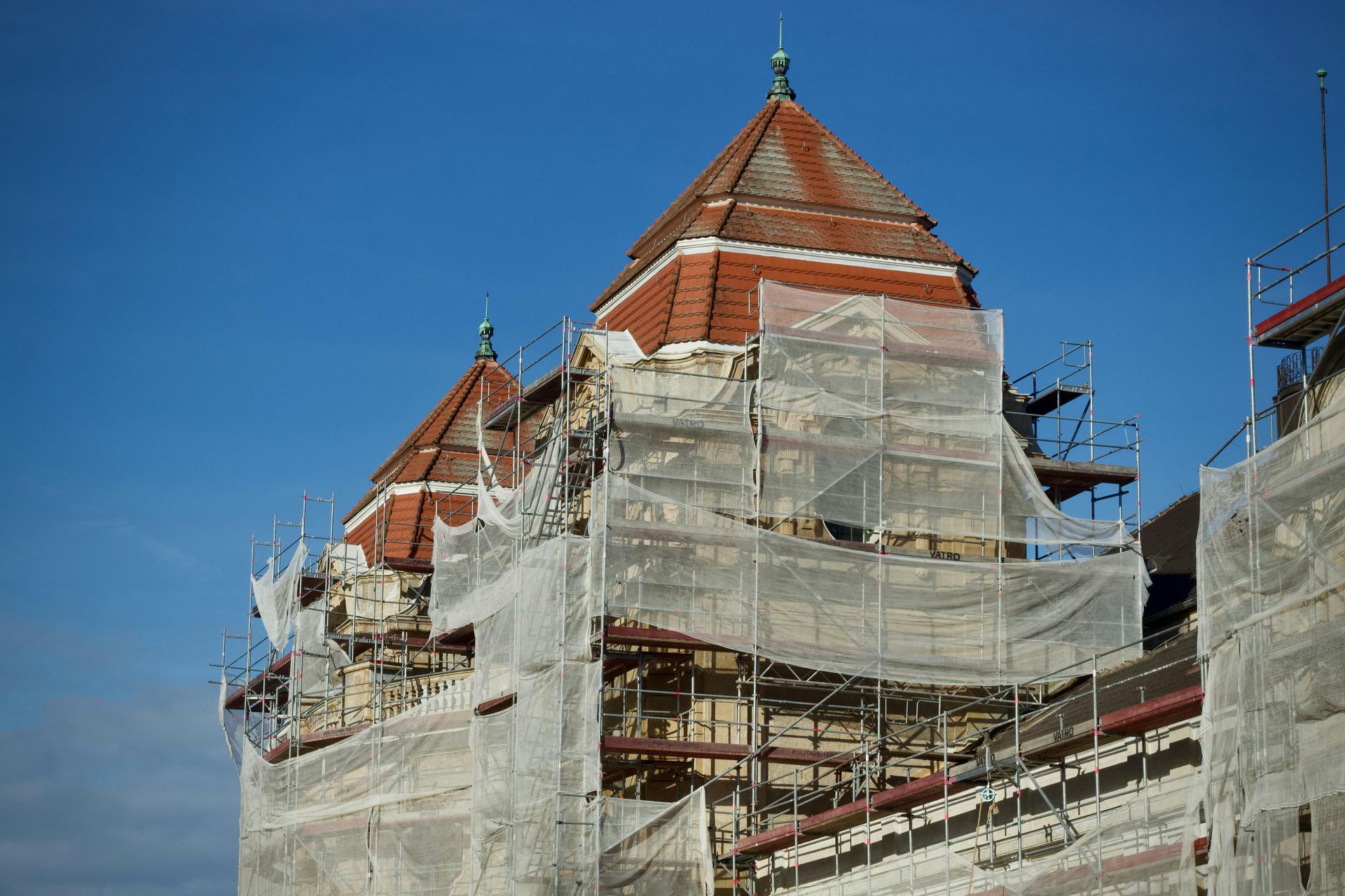Historic building under renovation, covered in scaffolding and white netting beneath a blue sky