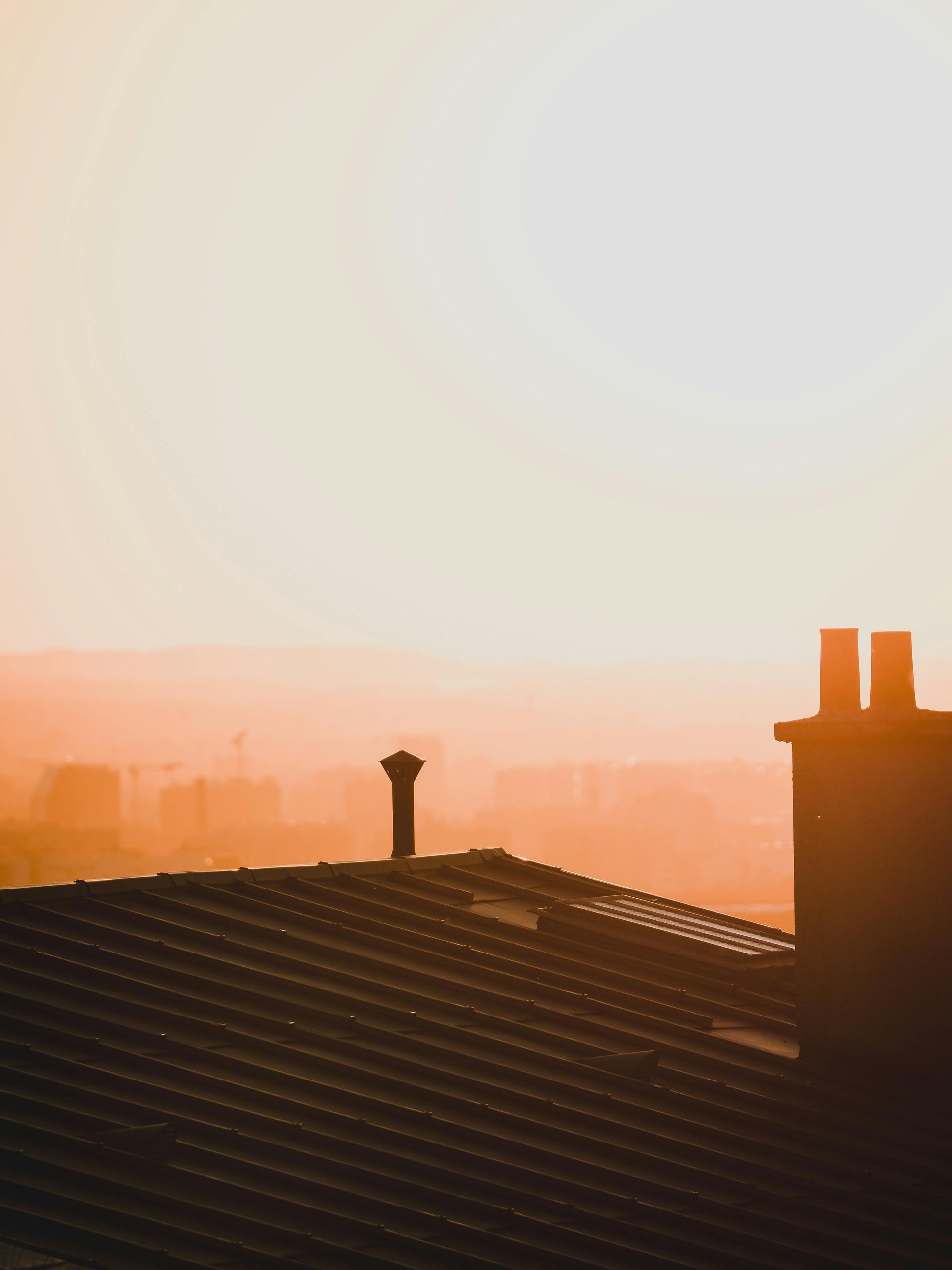 Sunrise over rooftops with orange haze and silhouetted chimneys