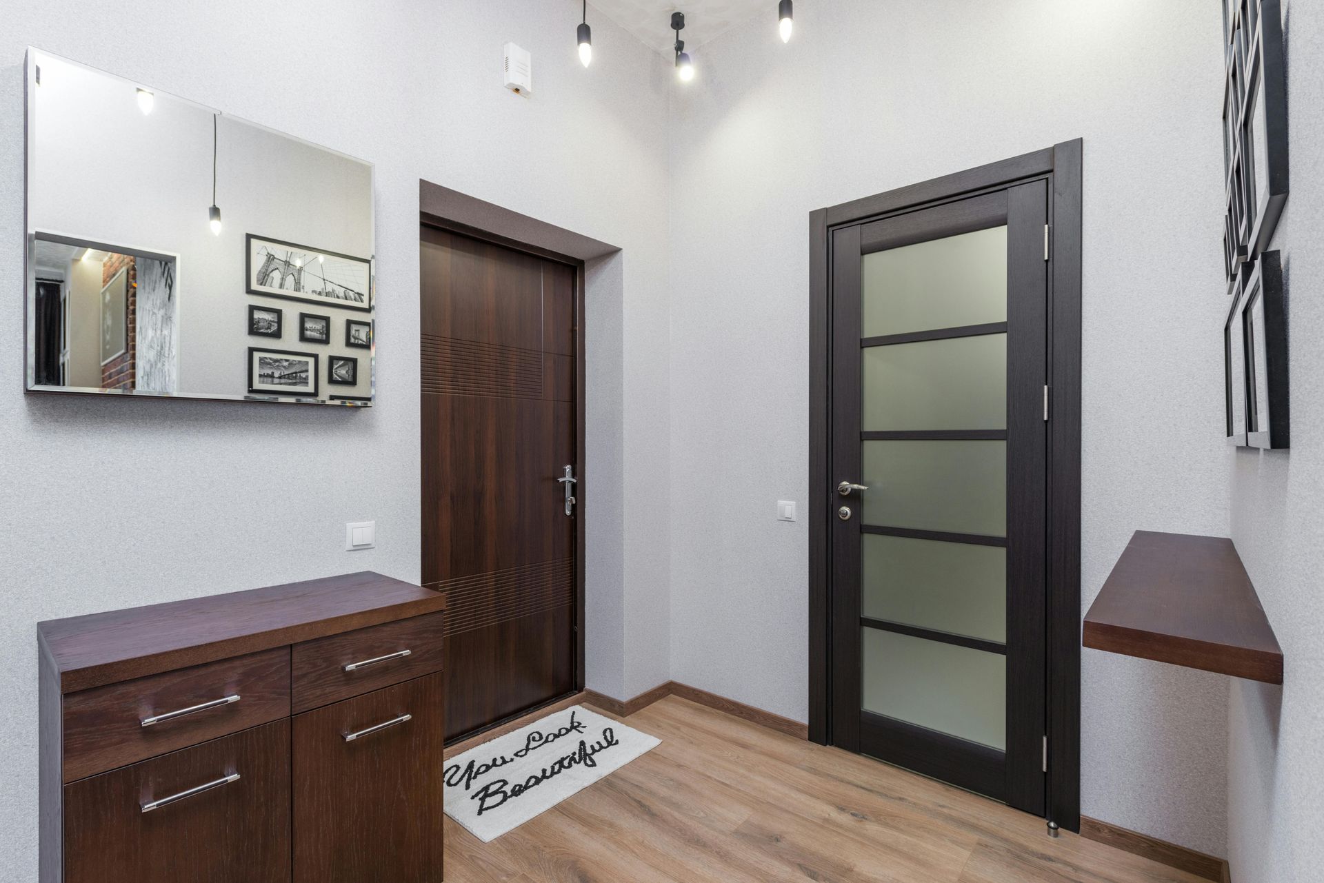 Modern entryway with two doors, wooden floor, mirror, and small cabinet on the left.