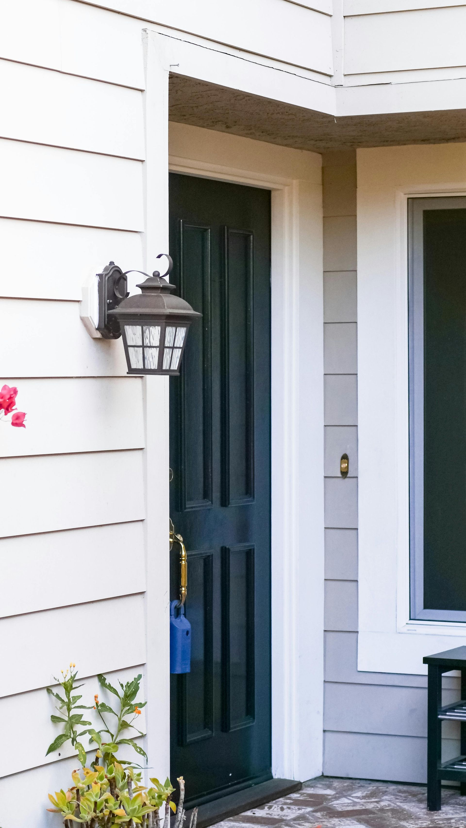 Front porch with a dark green door, wall lantern, and white siding beside a window.