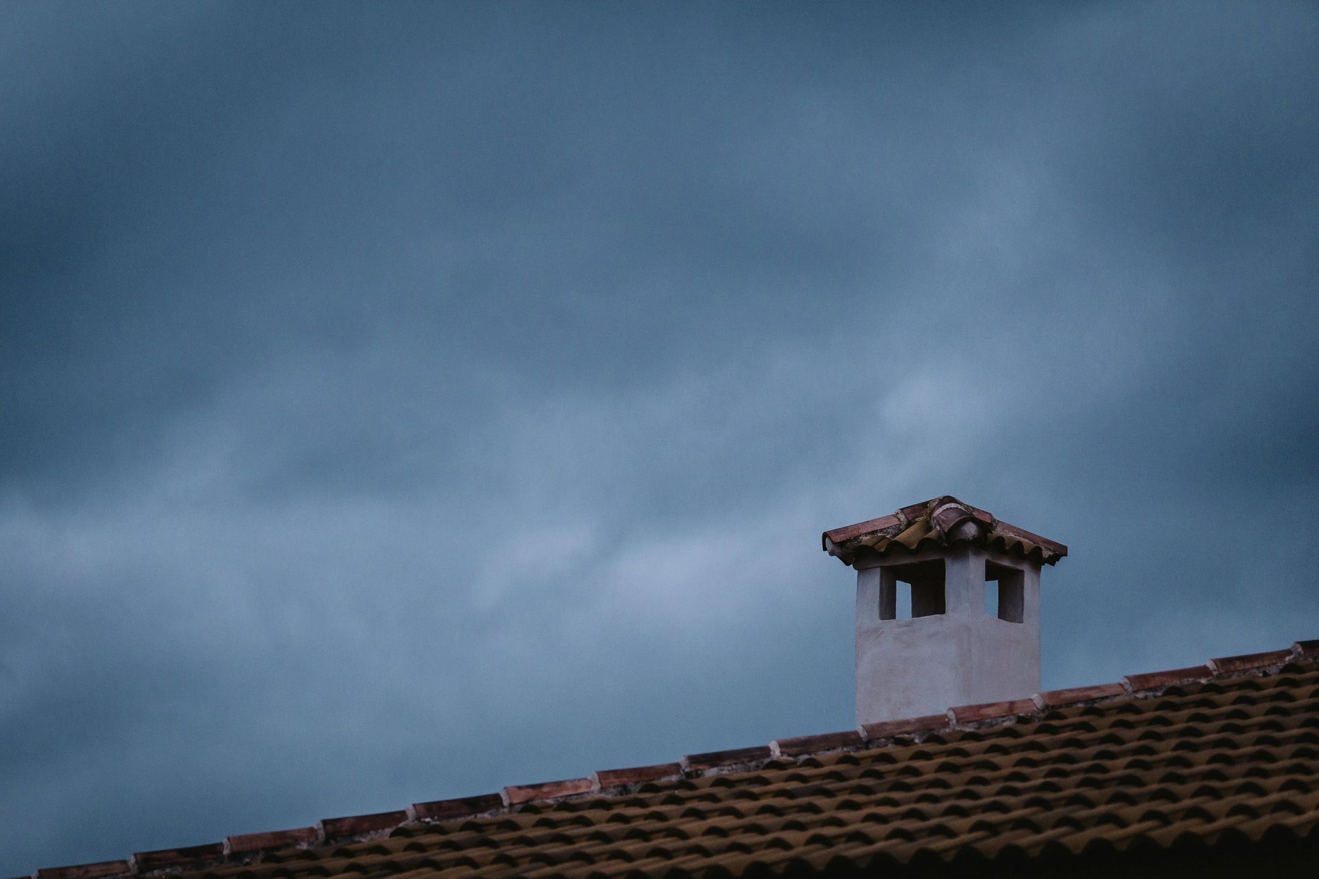 Dark stormy sky over a tiled rooftop with a chimney.