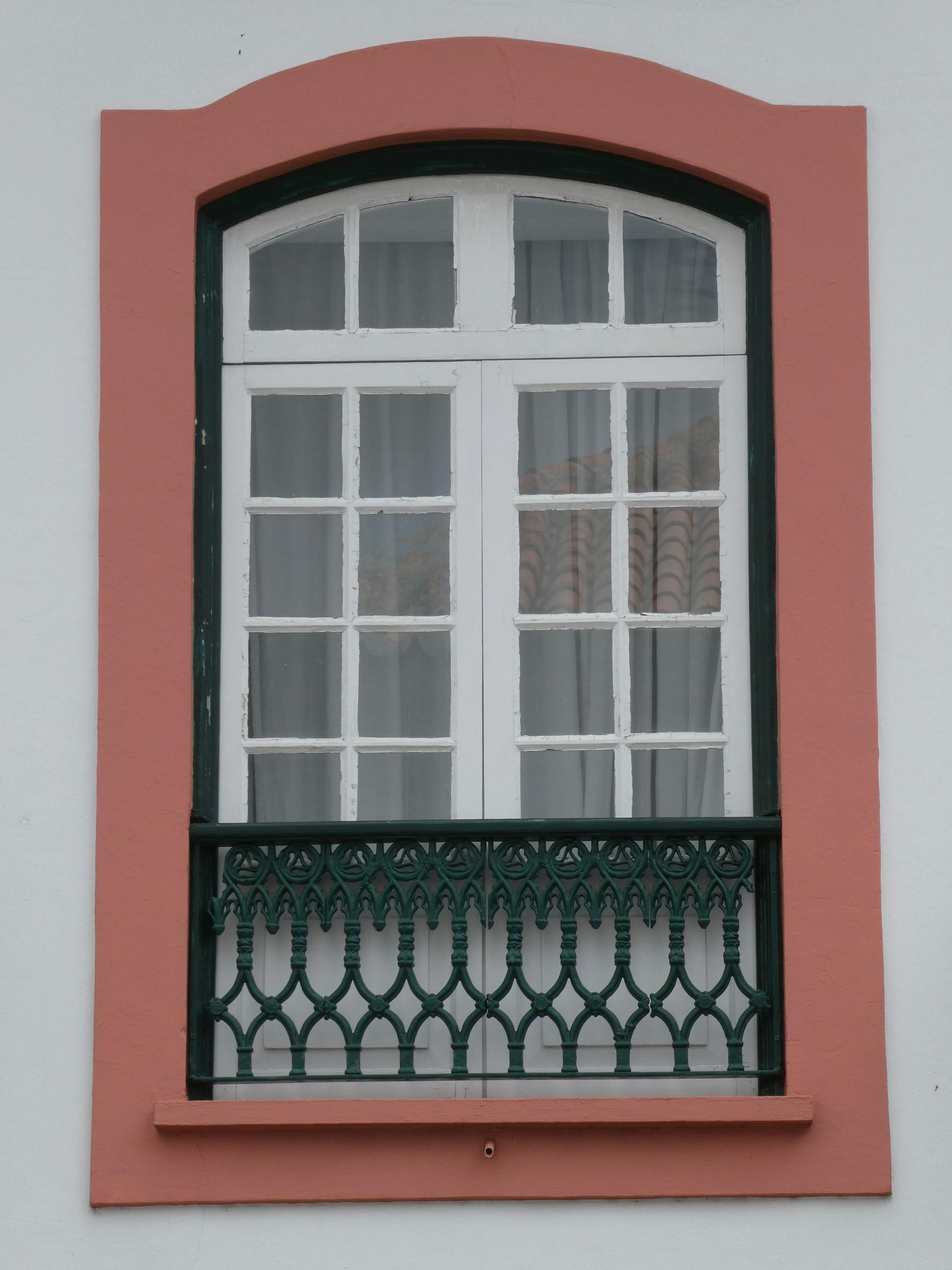Pink framed window with white panes and a black decorative balcony railing