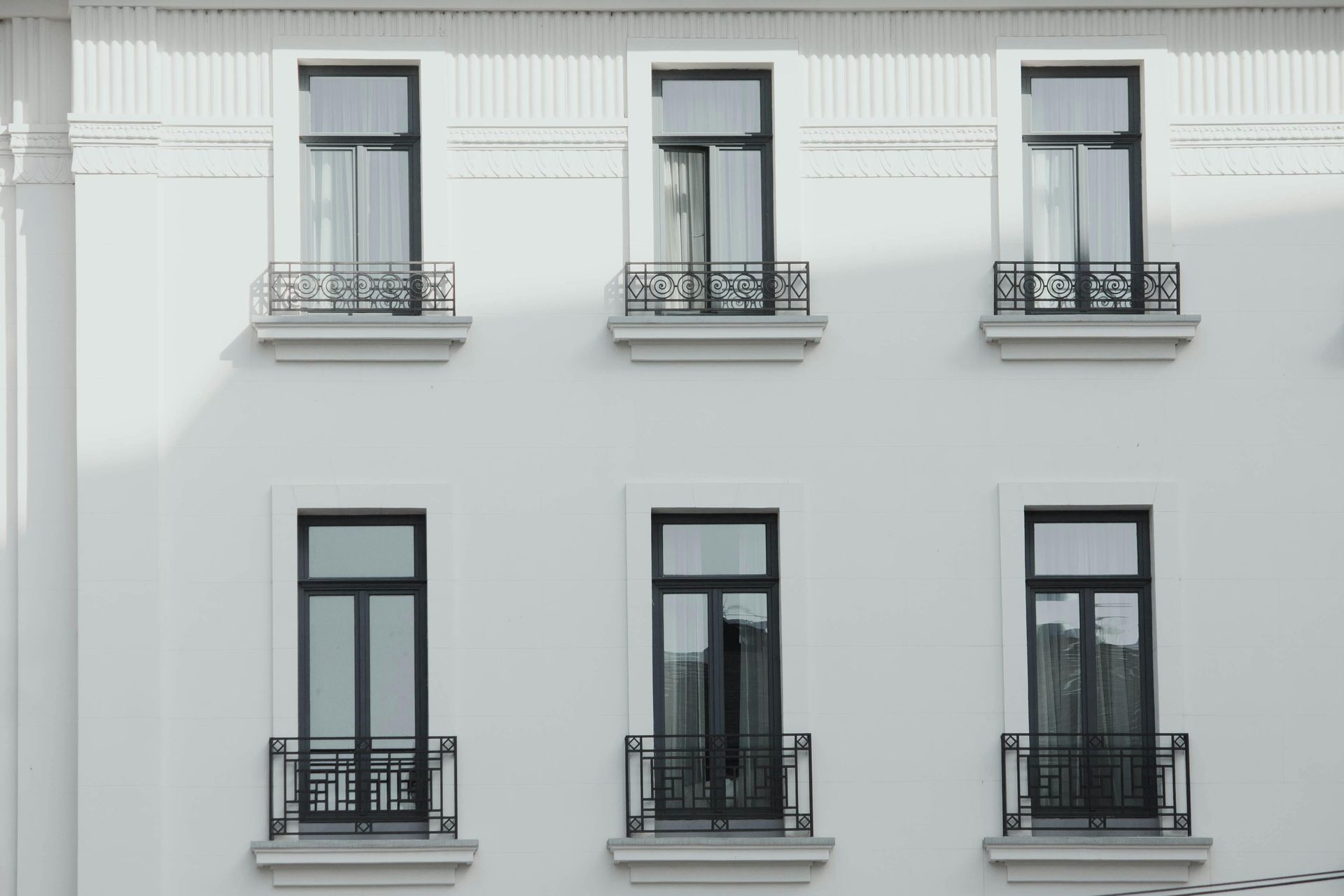 White building facade with six black-framed windows and small wrought-iron balconies