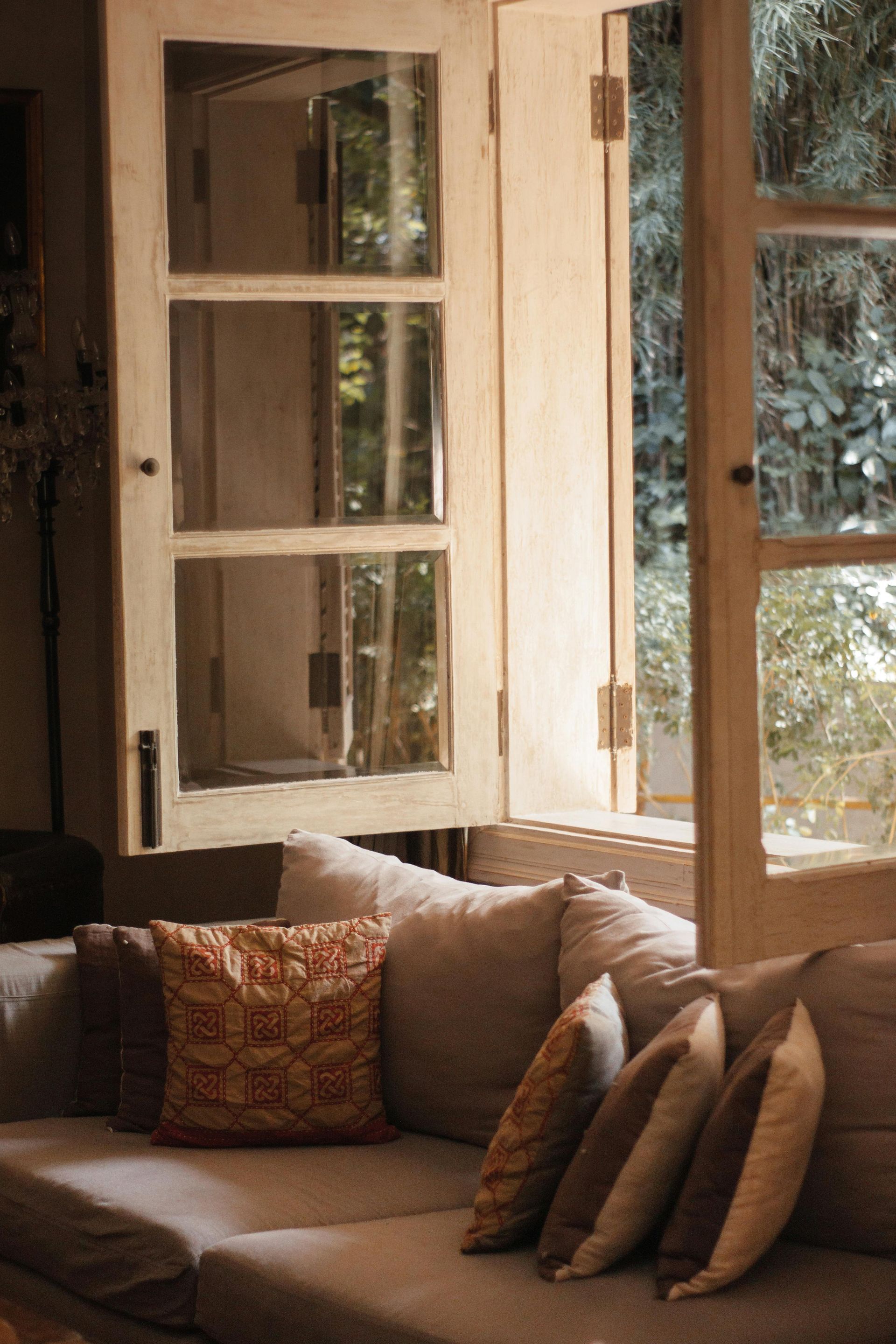 Cozy beige sofa by open wooden windows in a sunlit living room