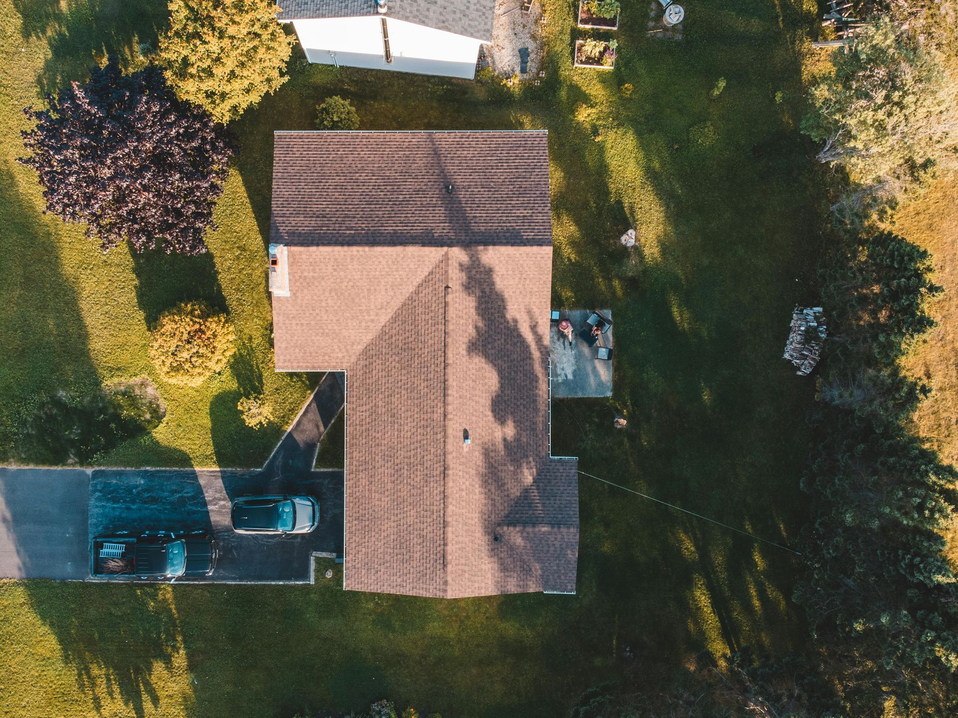 Aerial view of a house with a brown roof, backyard pool, and surrounding trees and lawn