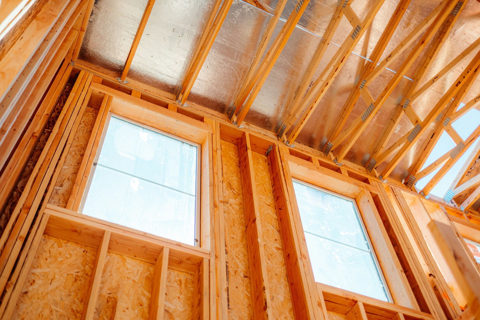 Unfinished wooden room framing with tall windows and exposed beams, viewed upward from inside