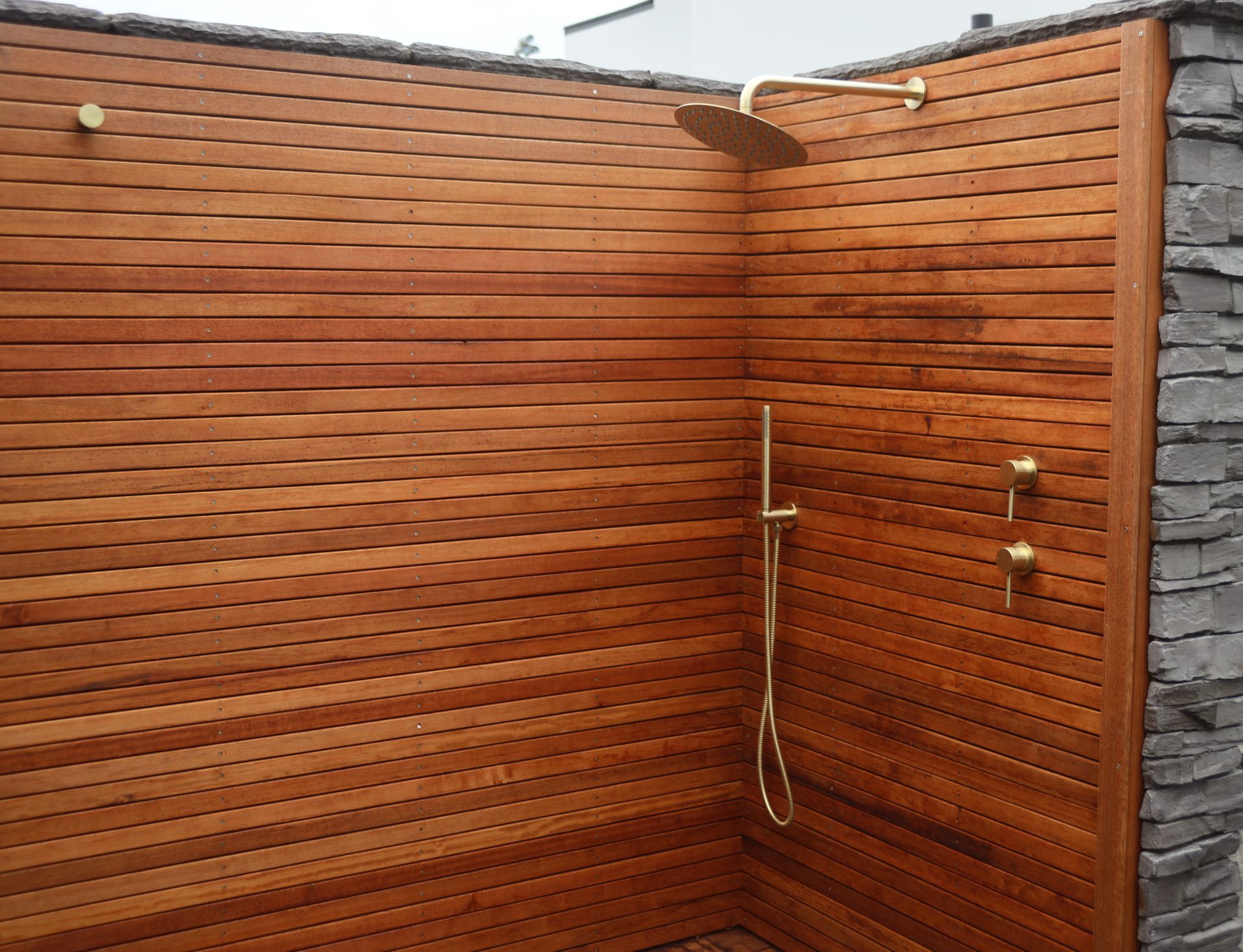 A wooden shower with a brass shower head