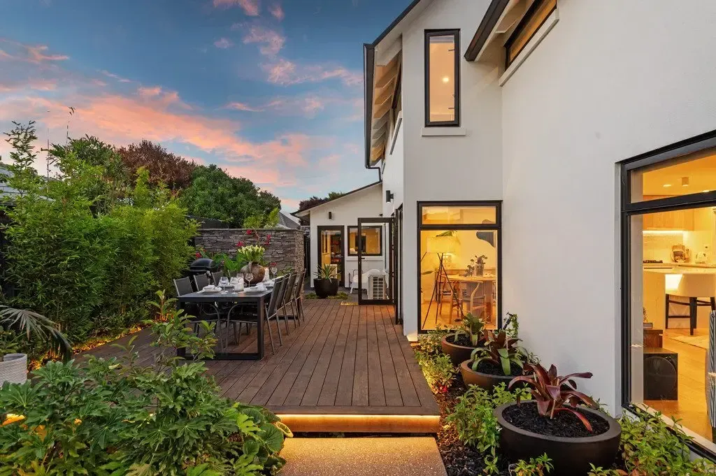 Backyard patio with a dark table, lush plants, and a white house at sunset.