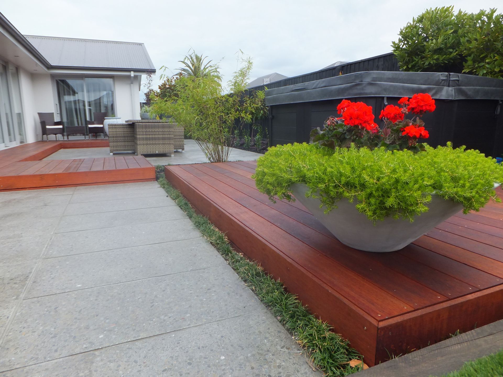 A planter with red flowers sits on a wooden deck