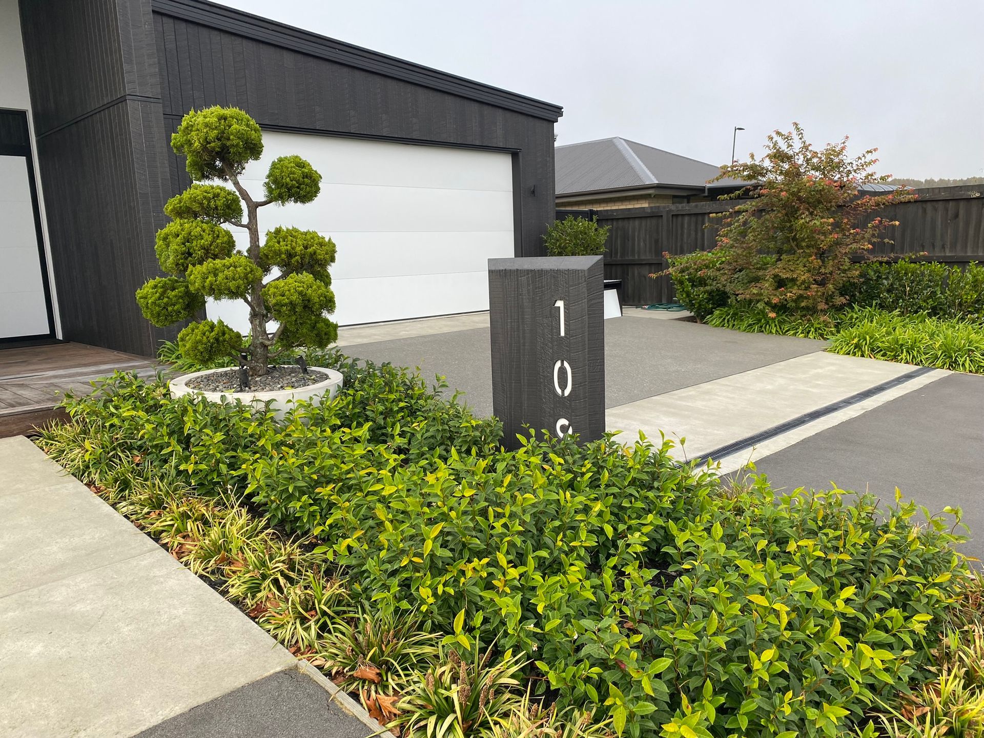 A planter with a tree in it is in front of a house.