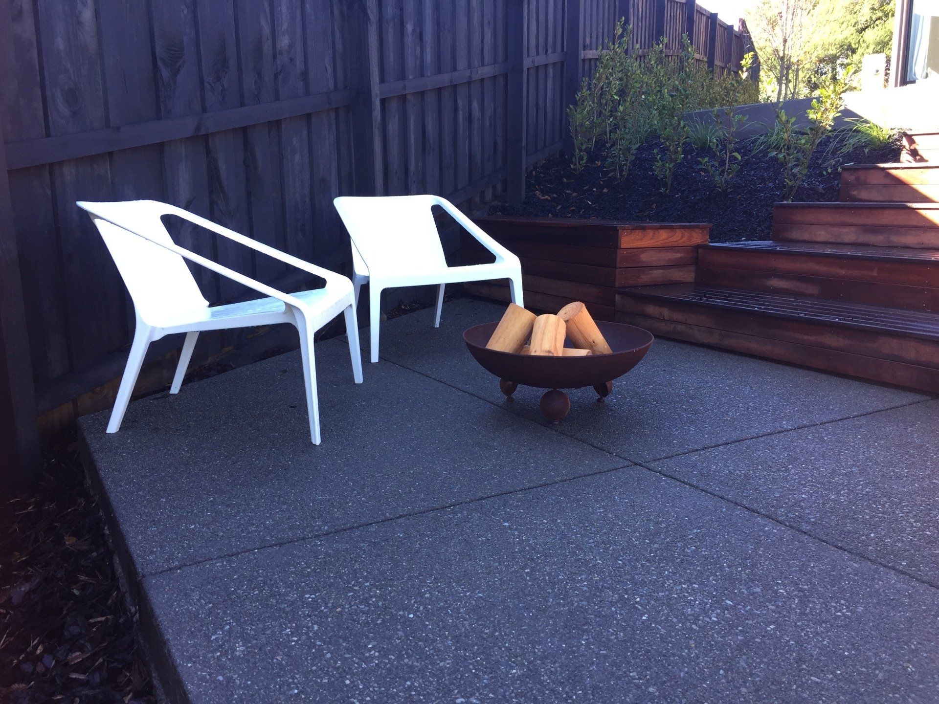 Two white chairs sit on a patio next to a fire pit