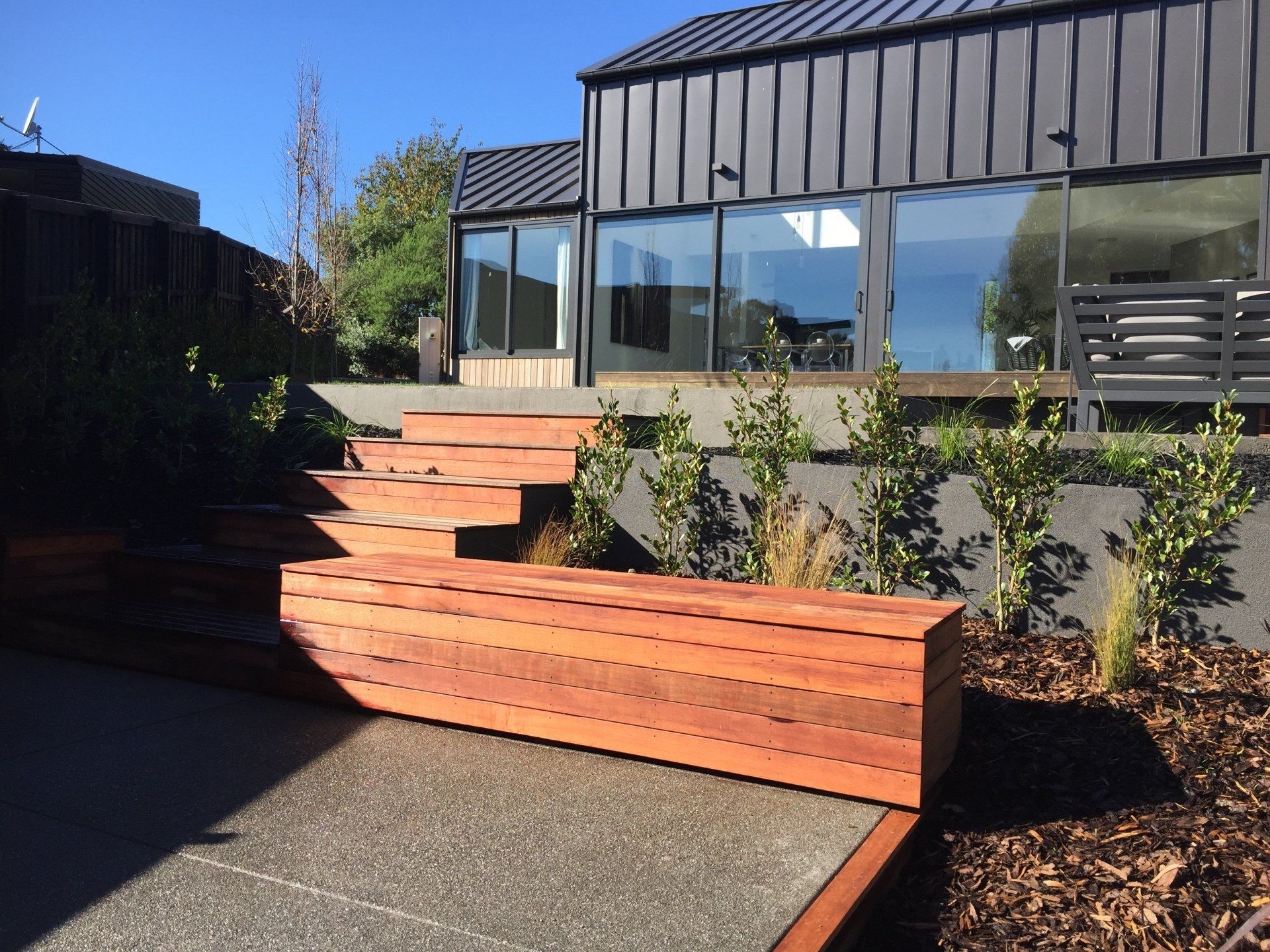 A wooden bench sits in front of a house with stairs leading up to it.