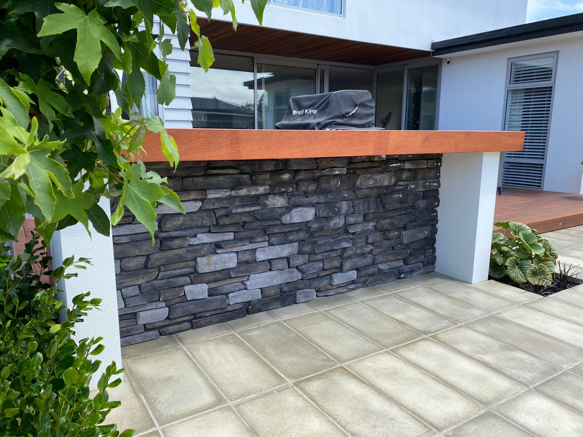 A brick wall with a grill on top of it in front of a house.