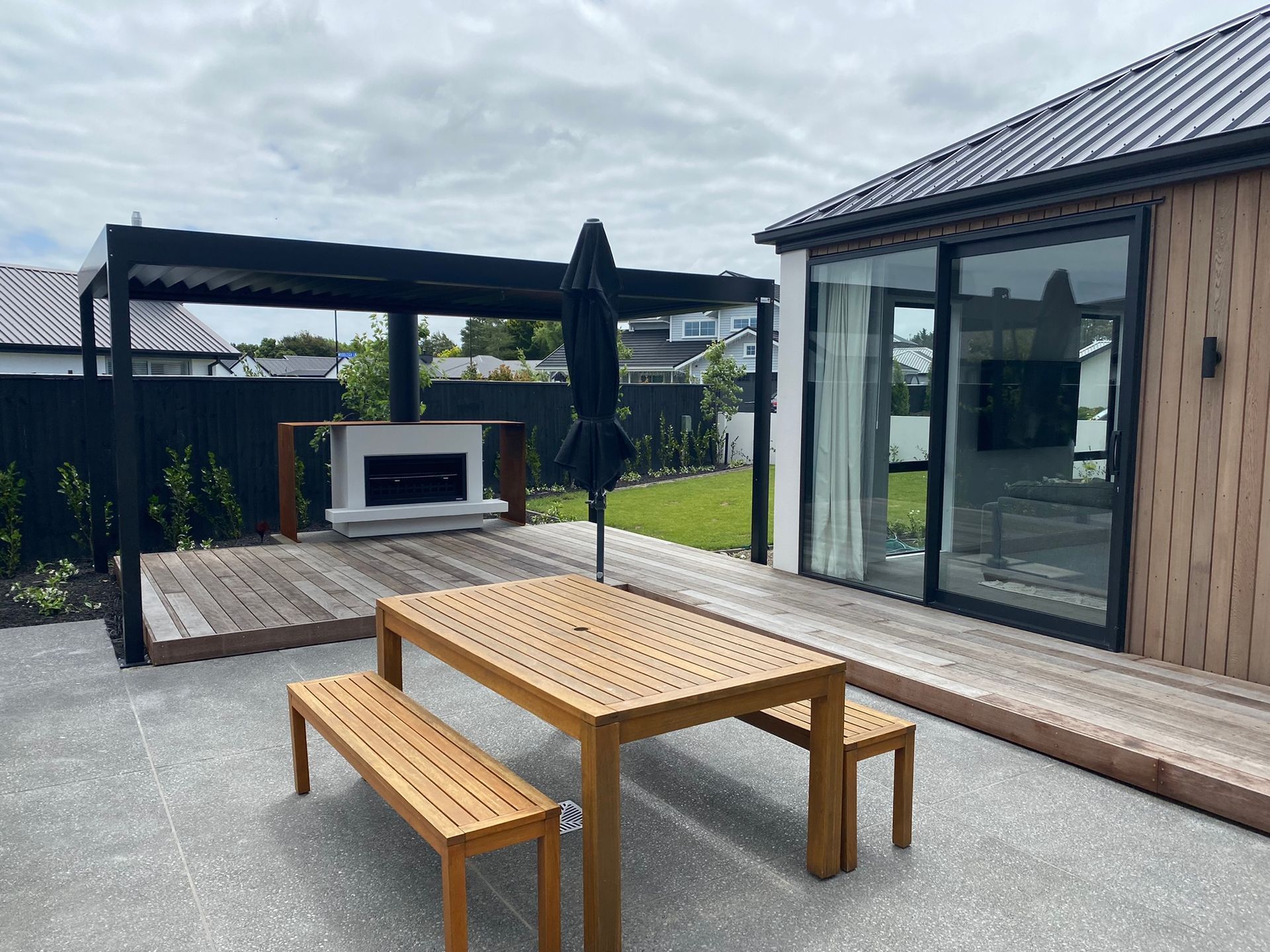 A wooden table and benches are on a patio in front of a house.