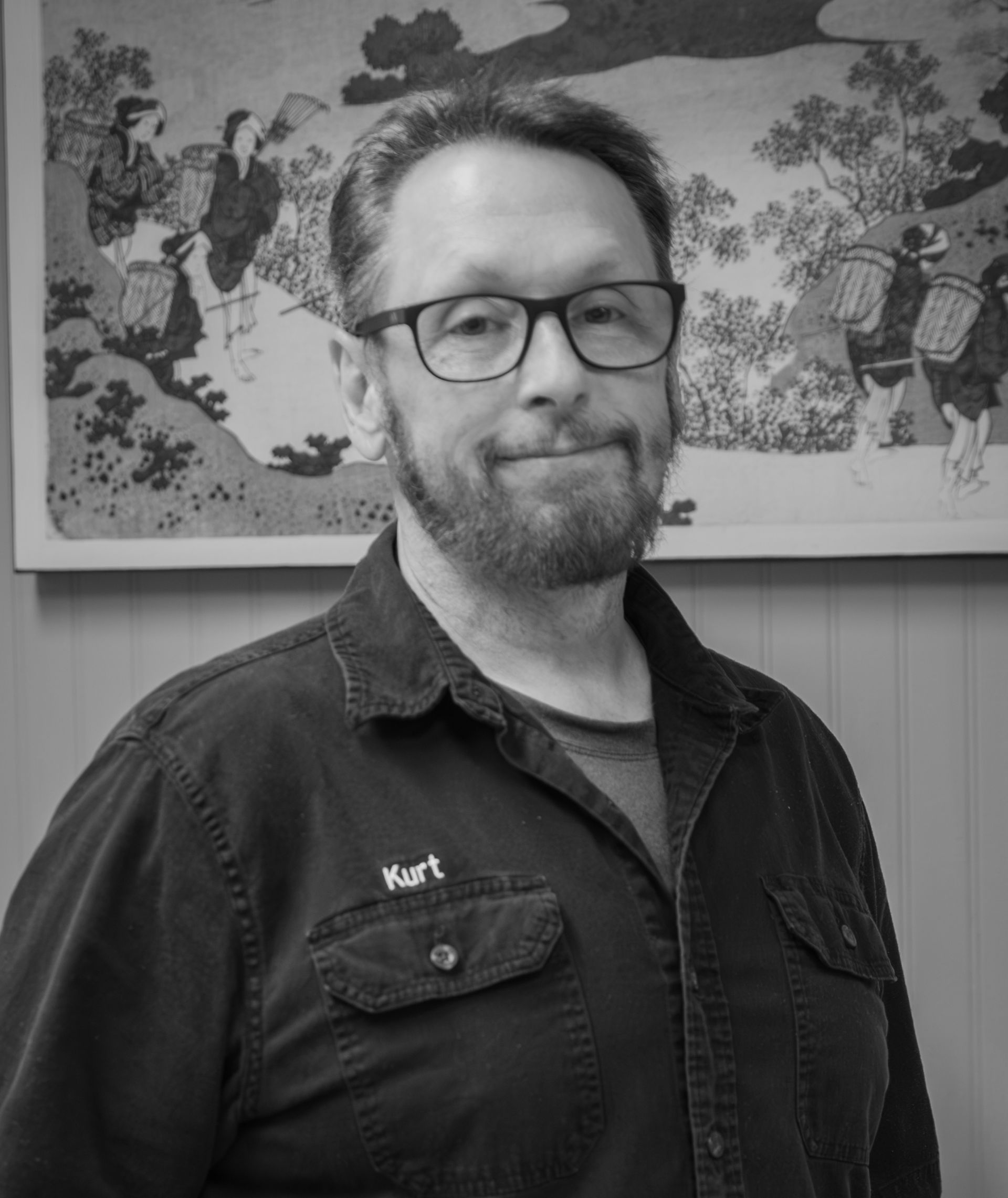 Man with glasses and beard, wearing a shirt with 