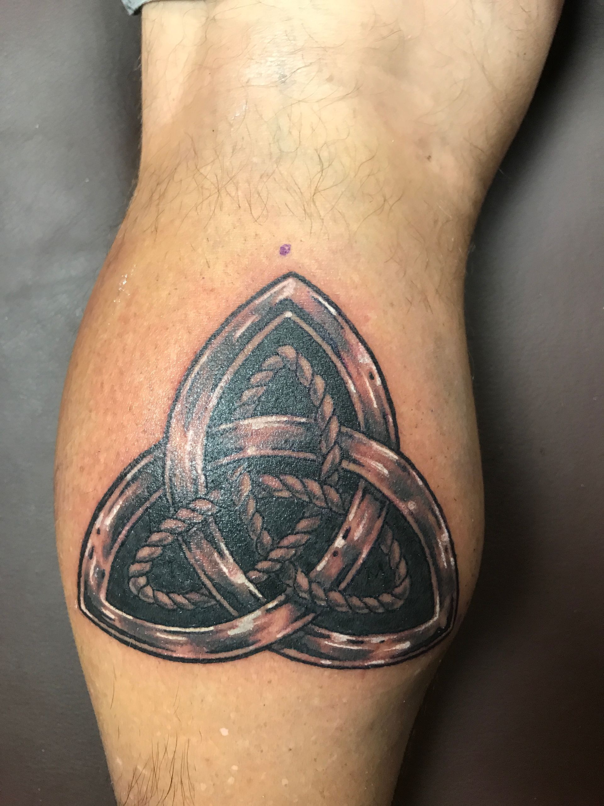 Tattoo of a Celtic knot design with a rope-like texture and metallic border on a leg.