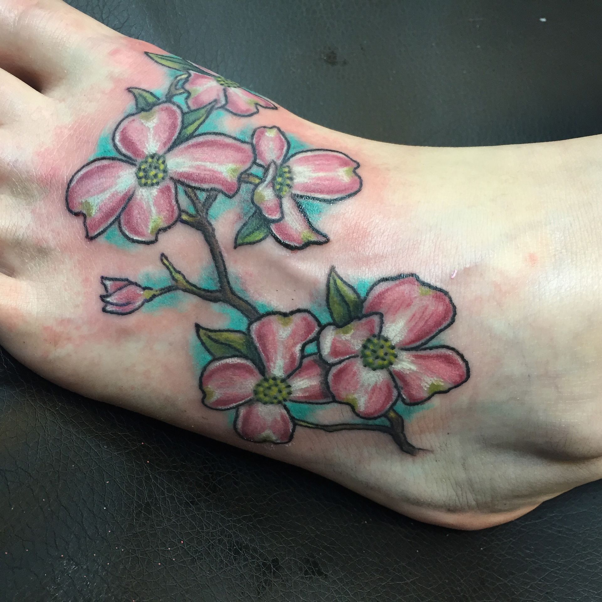 Dogwood flower tattoo on a foot, with pink petals, green centers, and turquoise background.