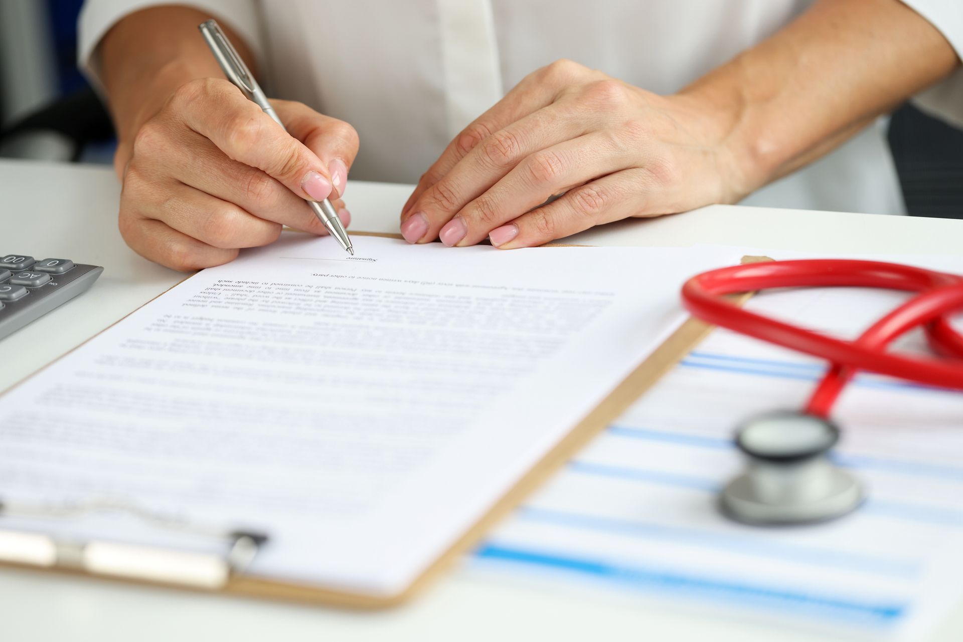 A doctor is writing on a clipboard next to a stethoscope.