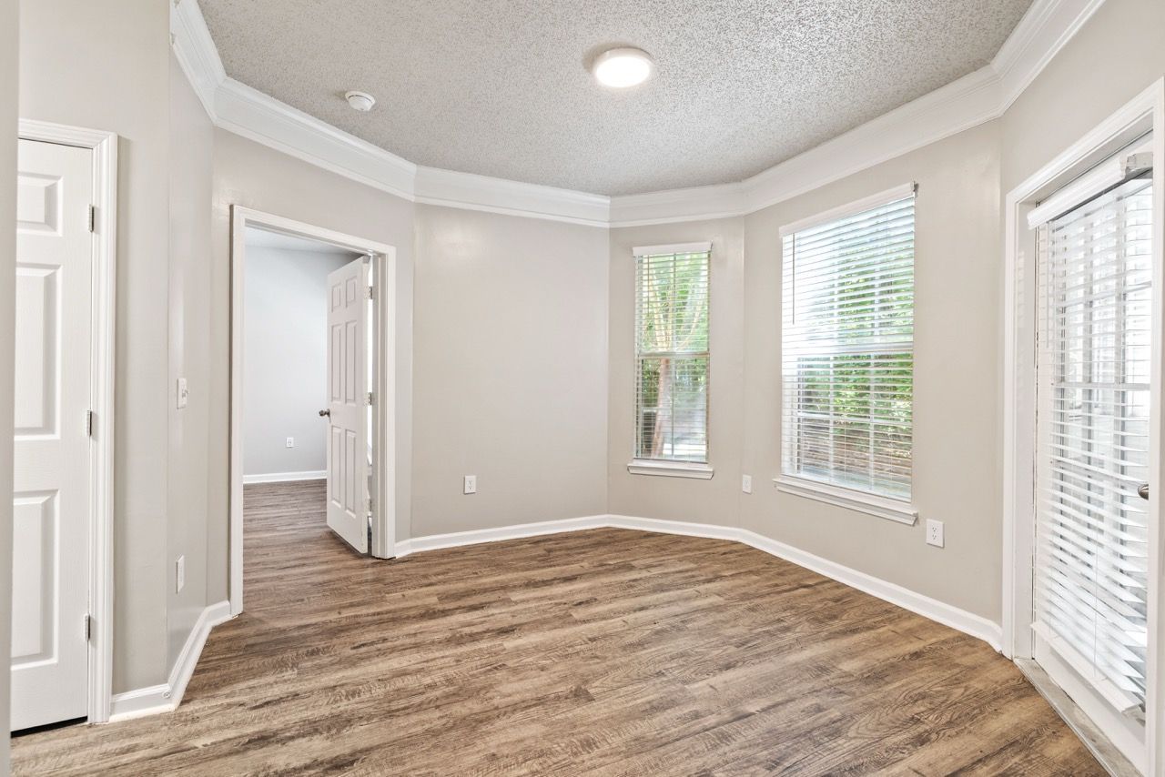 Unfurnished living room with light gray walls, white trim, and several windows with blinds.