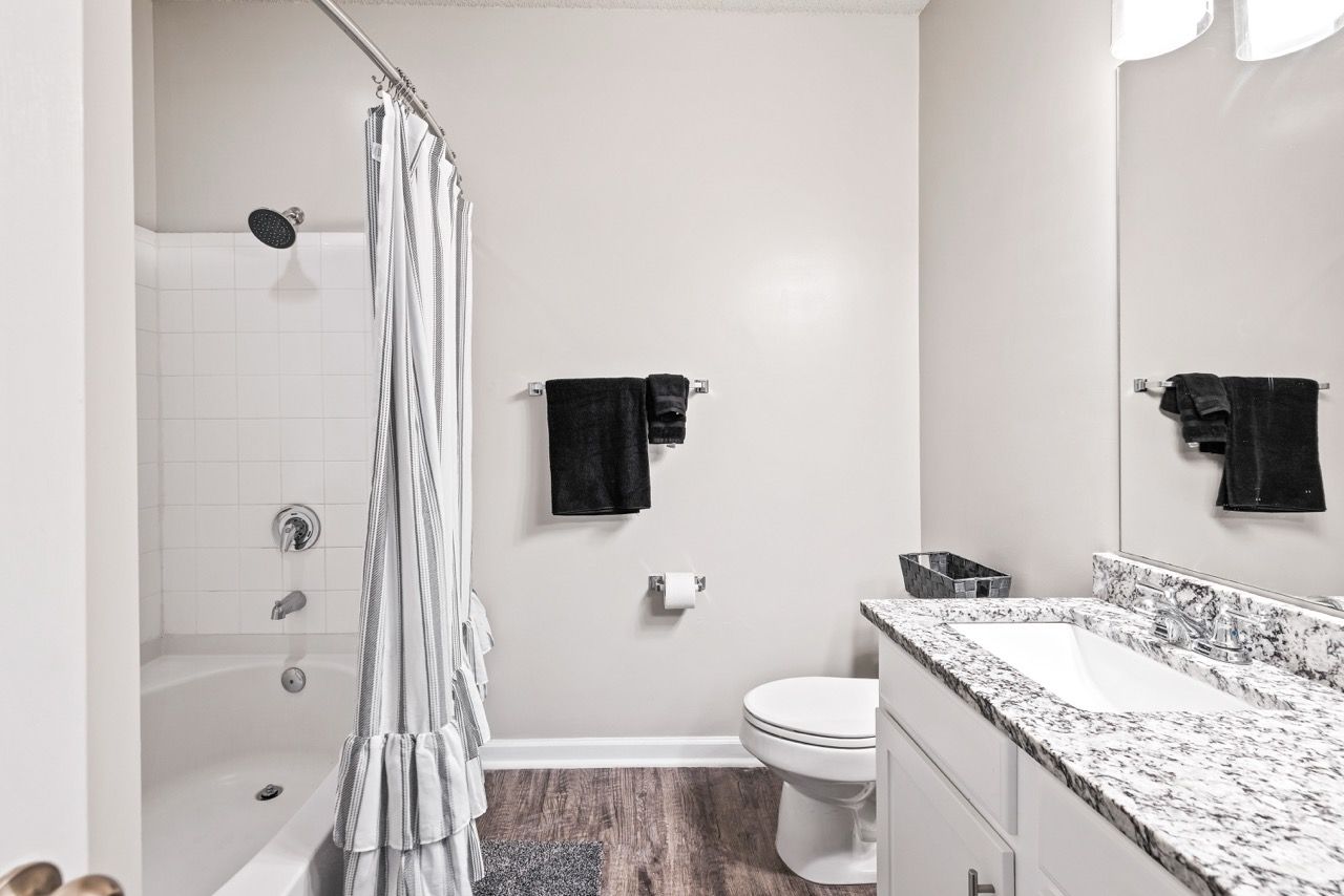 Bathroom with tub/shower, white tile, striped curtain, granite vanity, and a toilet.