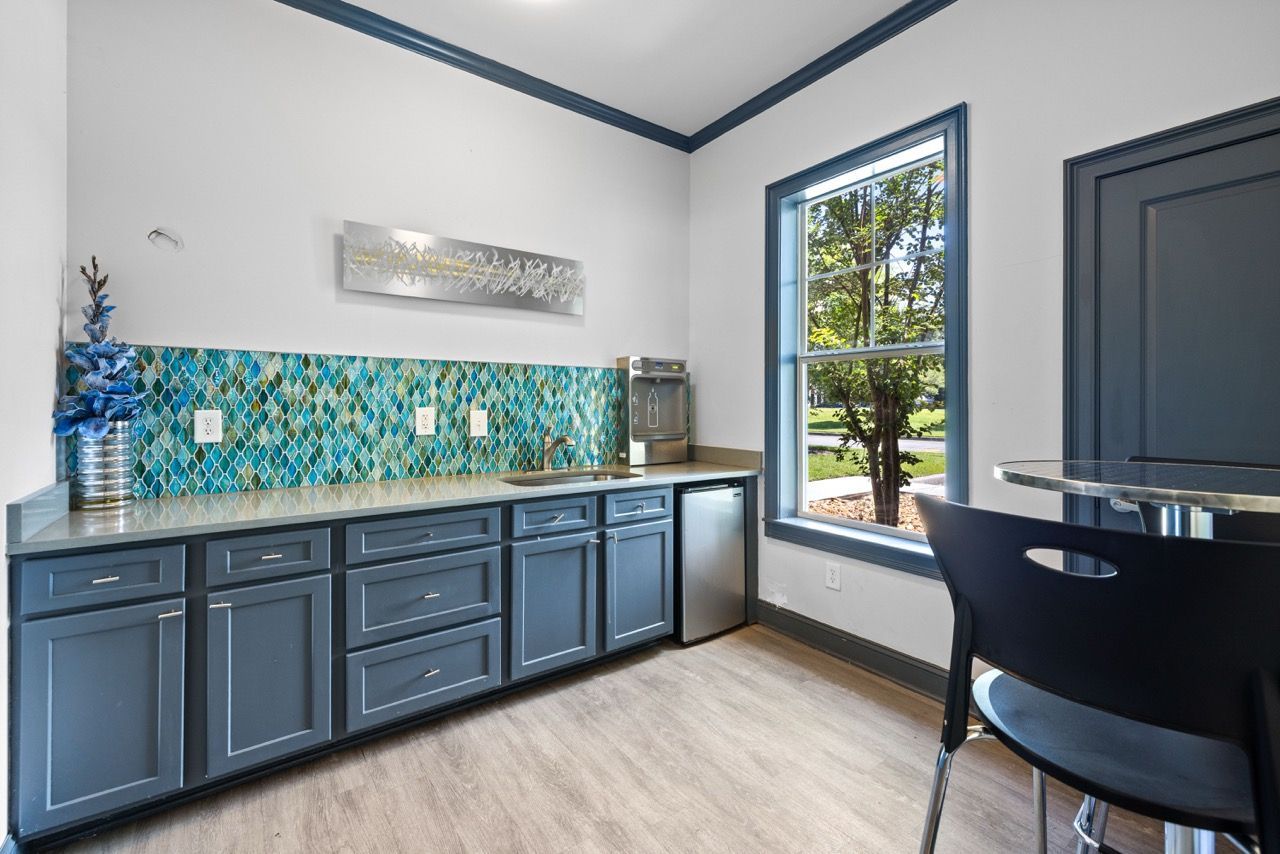 Blue kitchen cabinets with turquoise mosaic backsplash and a window view.