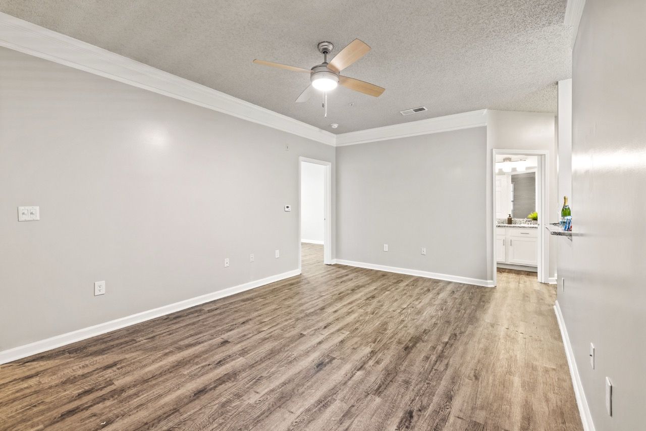 Empty living area in an apartment with gray walls, wood-look flooring, and a ceiling fan.