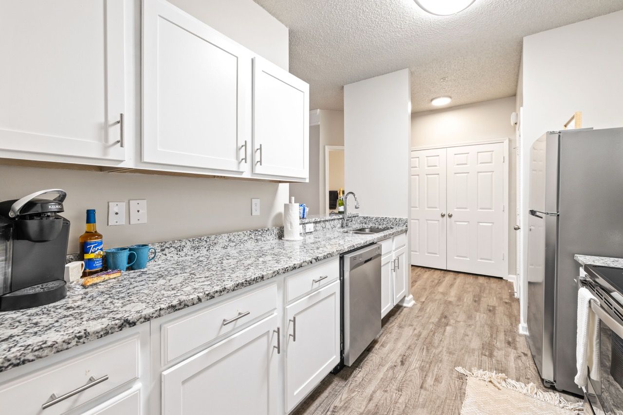 Bright kitchen in an apartment with white cabinets, granite countertops, and stainless appliances.
