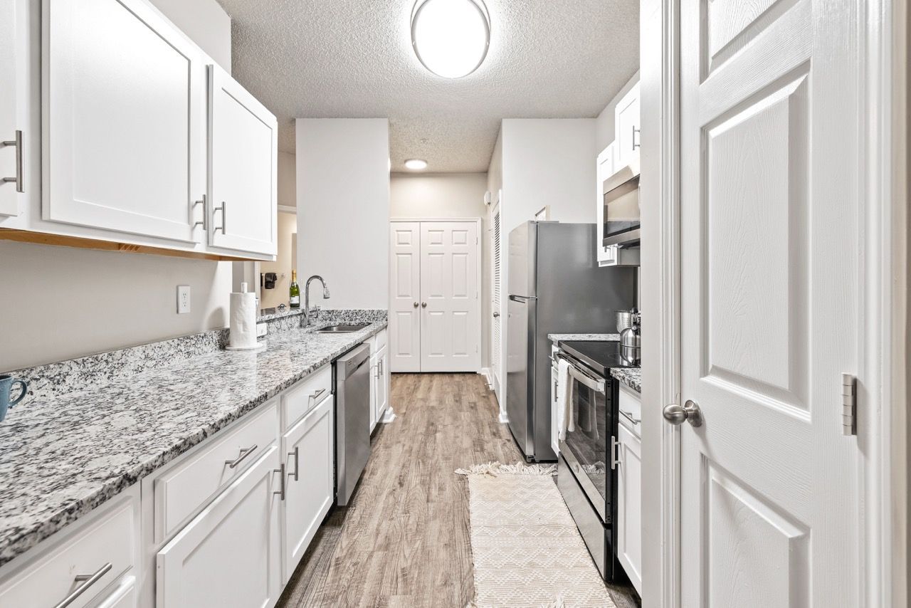 Narrow galley kitchen with white cabinets, granite countertops, and stainless steel appliances.