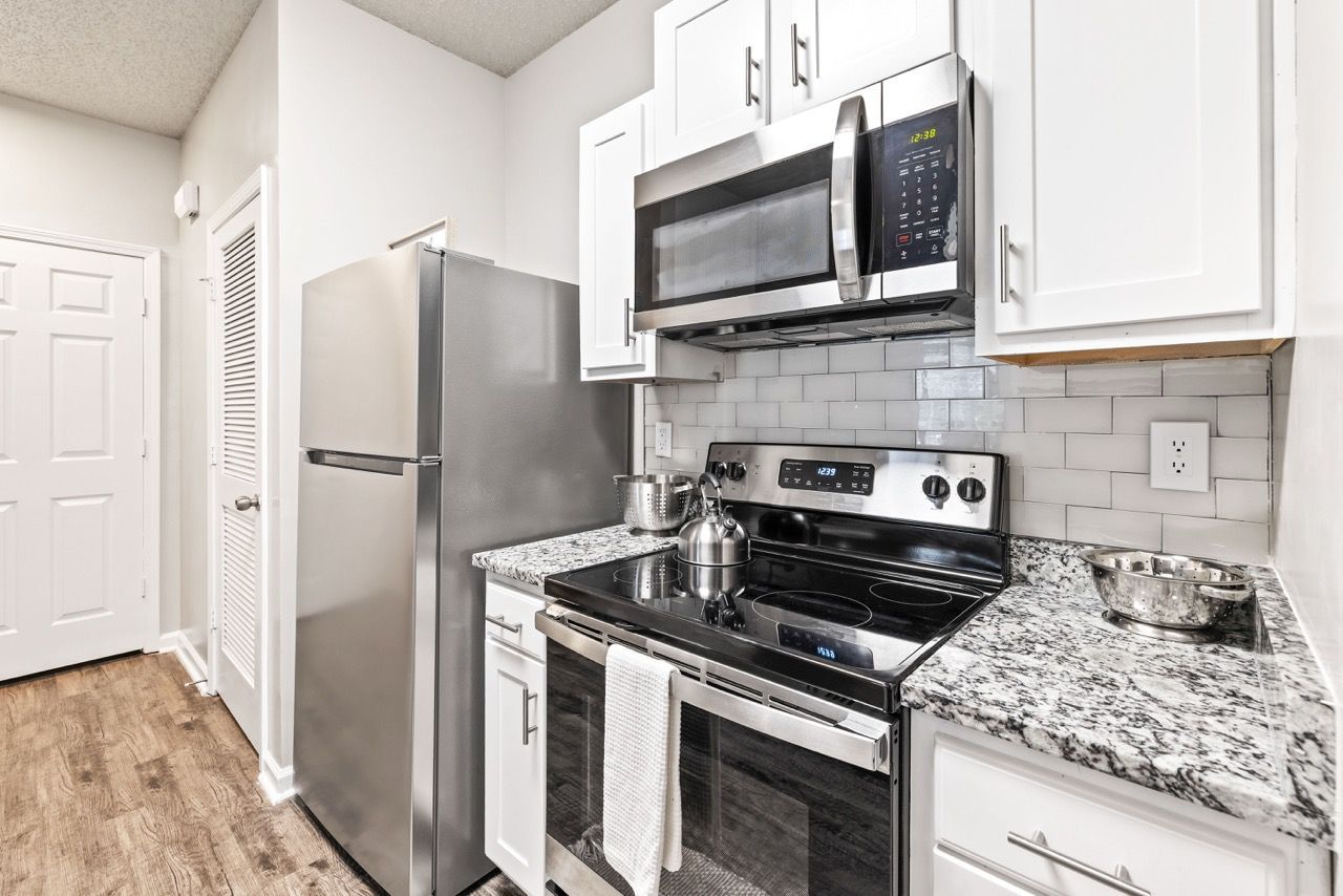 Kitchen with stainless steel refrigerator, microwave, stove, white cabinets, and granite countertops.