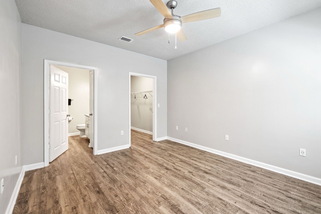 Empty bedroom with gray walls, wood-look flooring, ceiling fan, and doors to a bathroom and closet.