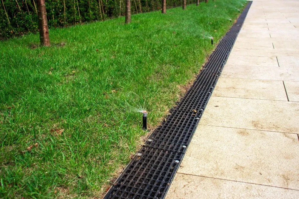 A drain on the side of a sidewalk next to a lush green field in McDonough, GA.