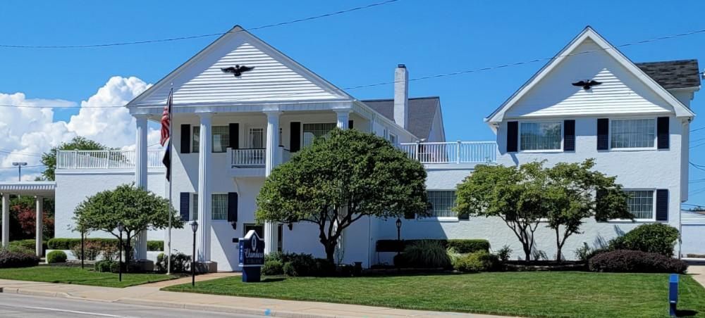 White building with columns, blue sky, green grass, trees.