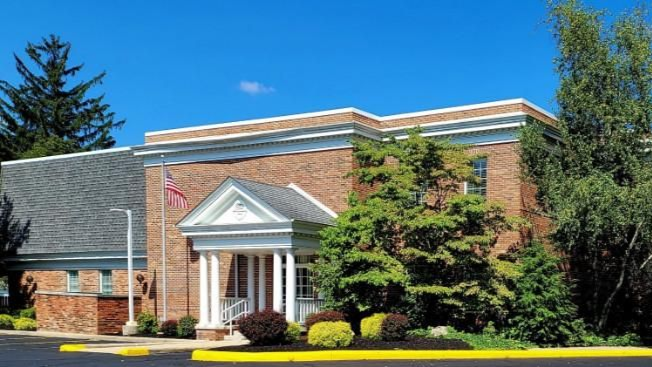 Red brick building with white columns, American flag, and green trees under a blue sky.