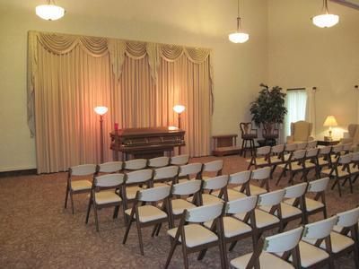 A funeral home chapel with folding chairs, a casket, curtains, and lamps.