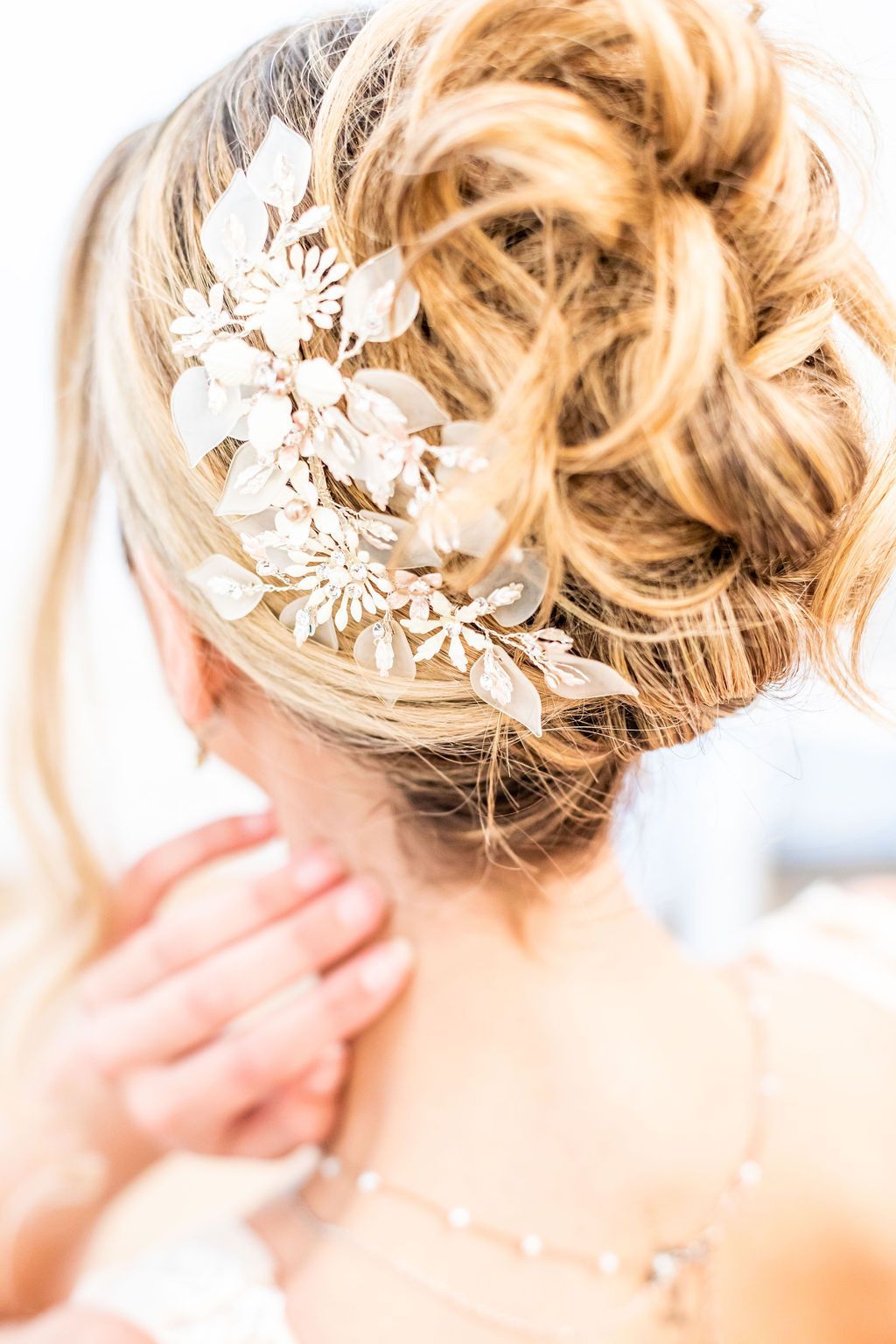 Blonde updo hairstyle with decorative white floral hairpiece.