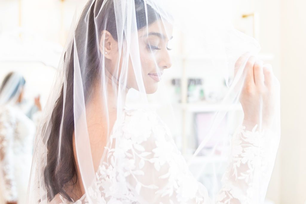 Woman in white lace dress adjusts sheer veil, side profile.