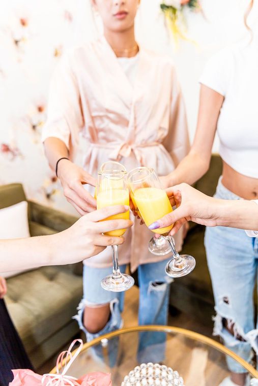 People in a room clink champagne flutes together; one person wears a pink robe.