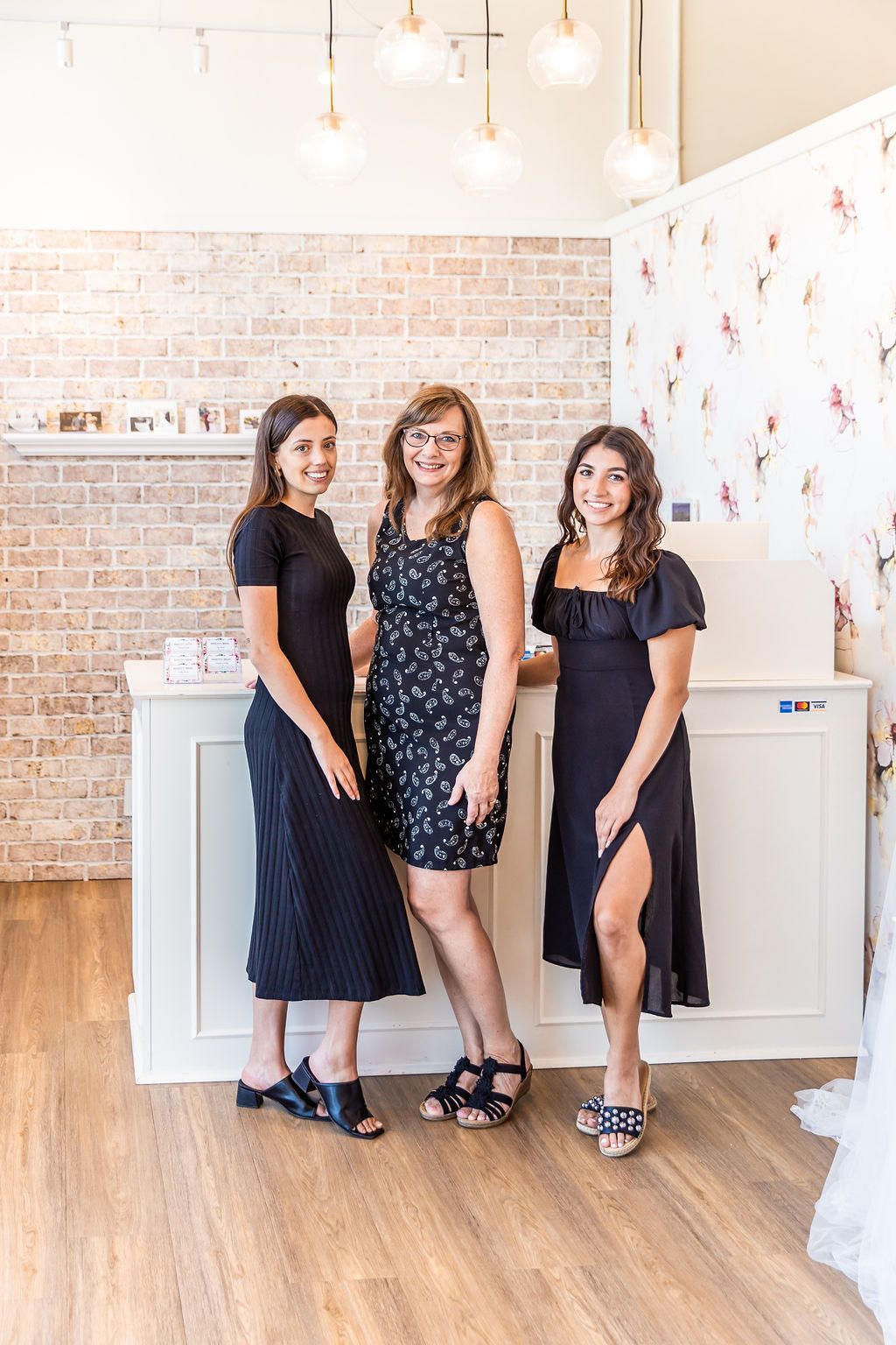 Three people pose behind a counter in a boutique. T
