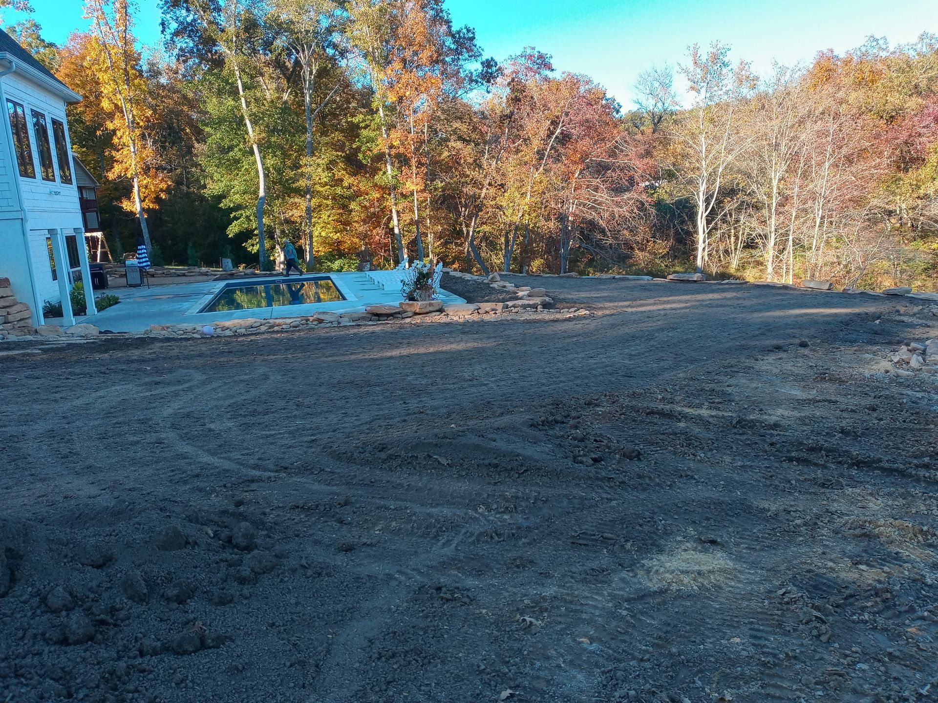 A white house is sitting in the middle of a dirt field surrounded by trees.