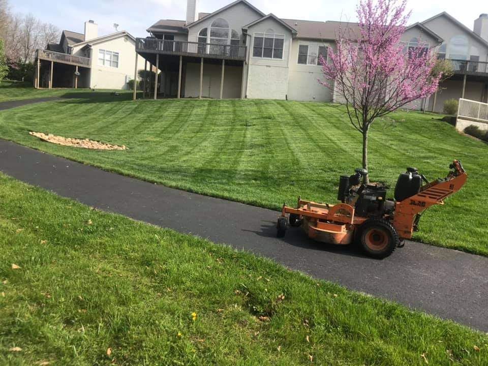 A lawn mower is cutting a lush green lawn in front of a house.