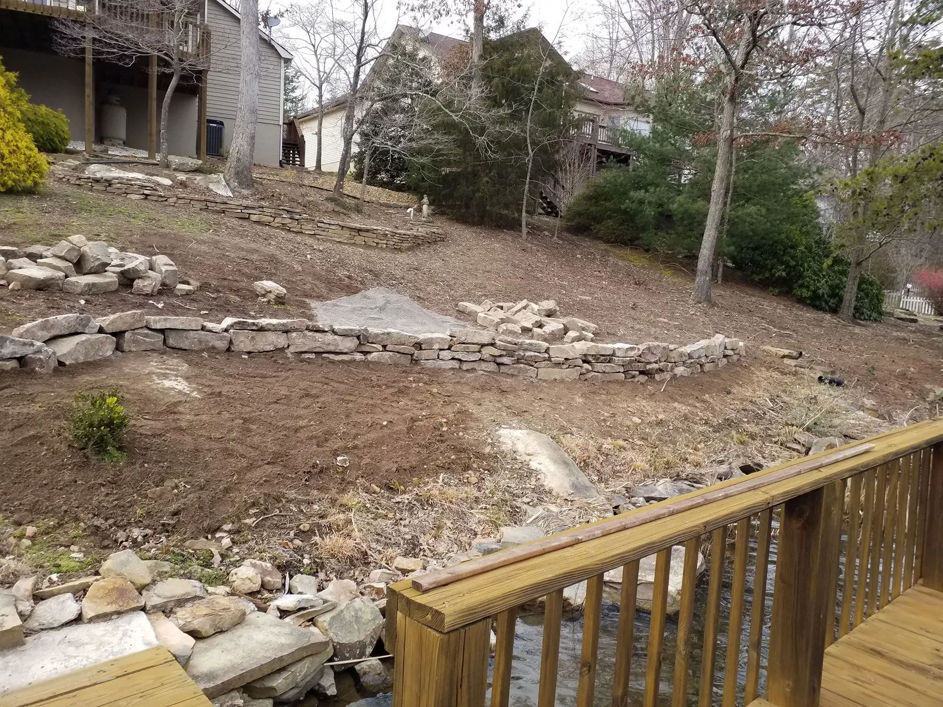 A wooden deck overlooking a rocky yard with a house in the background.