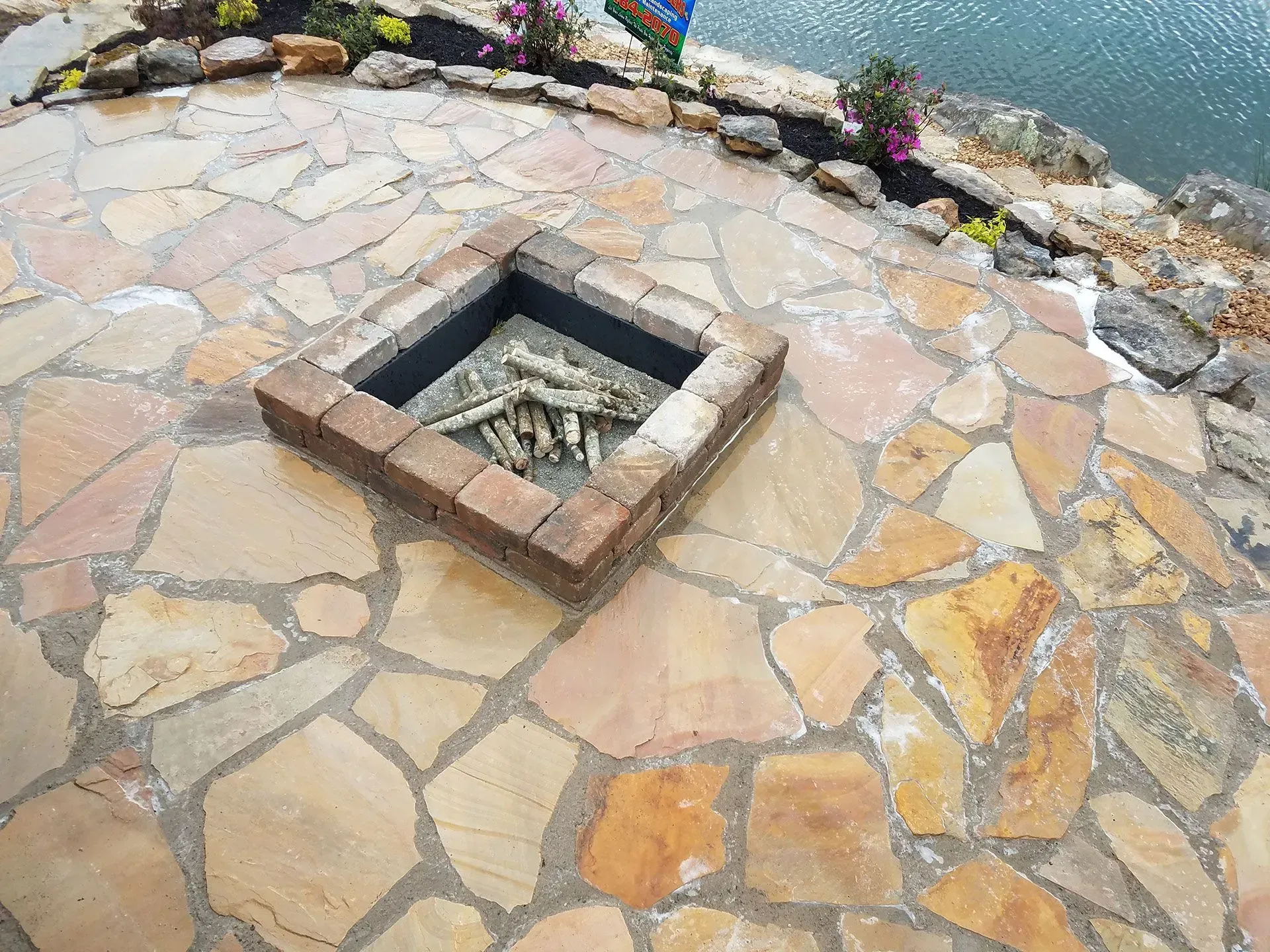A fire pit is sitting on top of a stone patio next to a body of water.