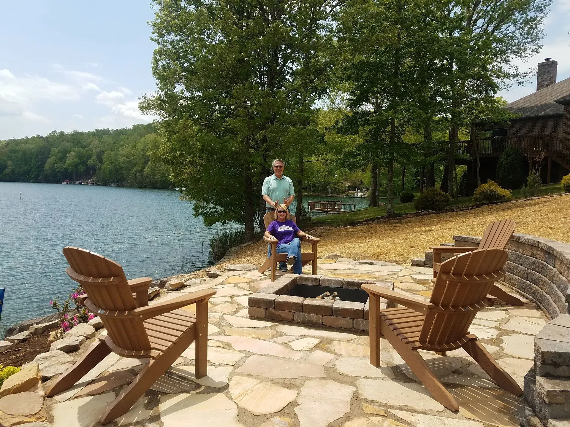A man and a woman are next to a fire pit by a lake.