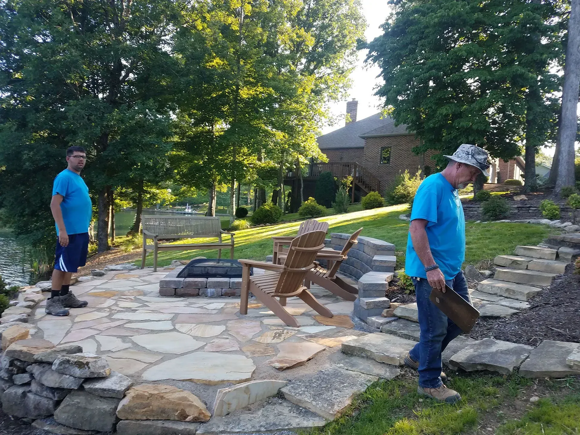 Two men are working on a stone patio in a backyard.