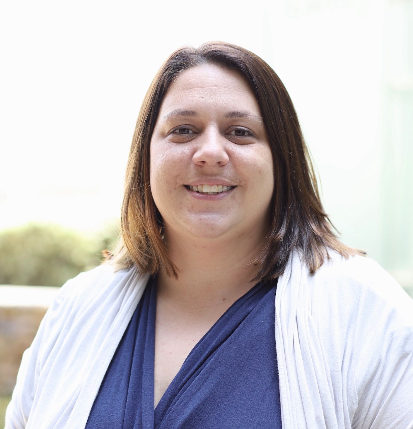 a woman wearing a blue shirt and a white sweater smiles for the camera