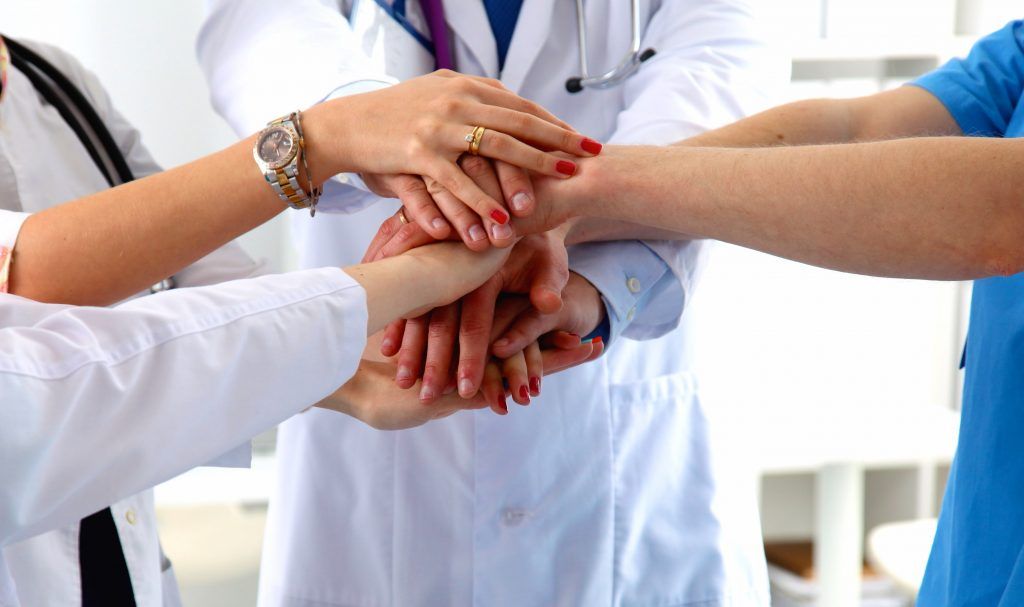 a group of doctors and nurses are putting their hands together .